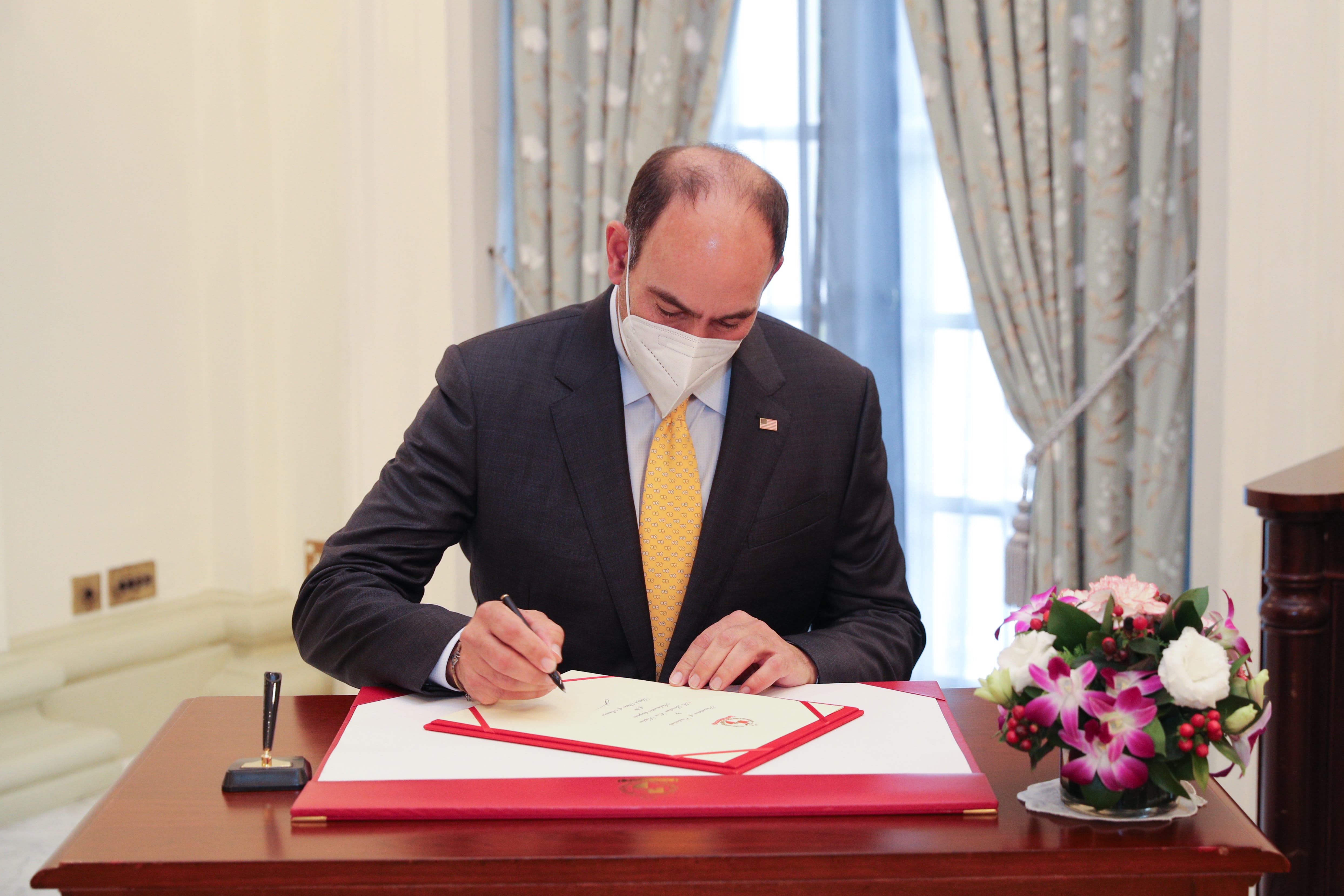 Man in suit and mask signs document on desk with flowers.