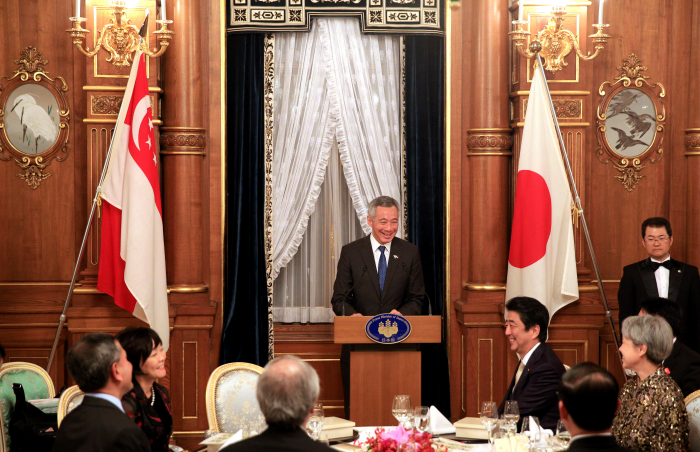 Lee Hsien Loong at podium with Singapore & Japan flags, seated guests, Shinzo Abe visible.