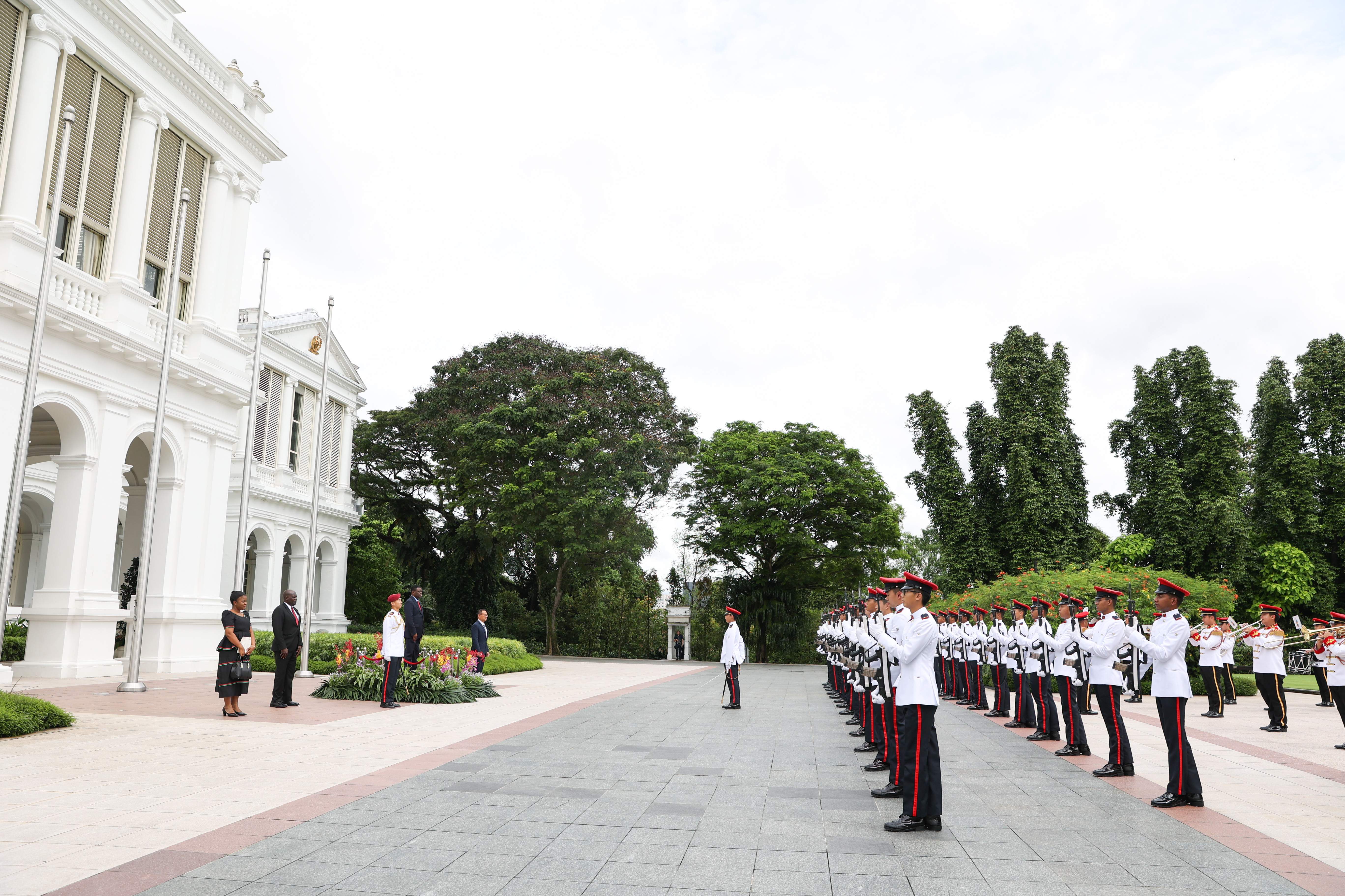 Honor guard in white uniforms and red hats stand at attention outside a white building.