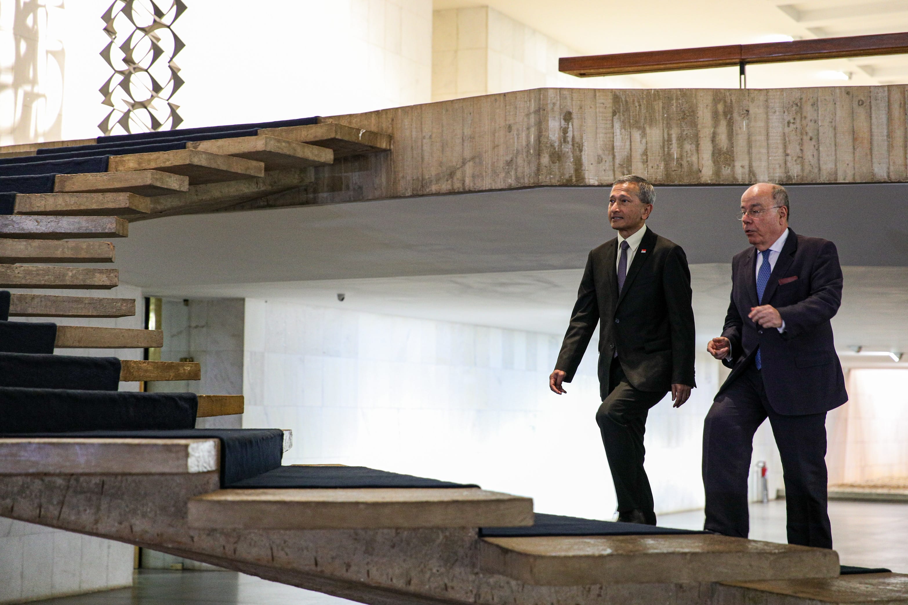 Two men in suits walking up a floating staircase with blue carpeting.