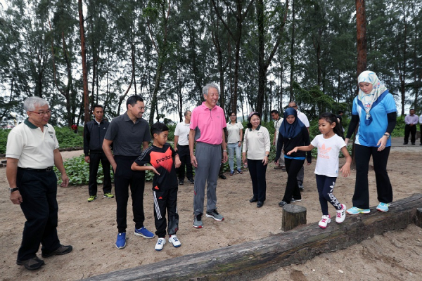 Lee Hsien Loong with others in a park, a girl walks on a log.