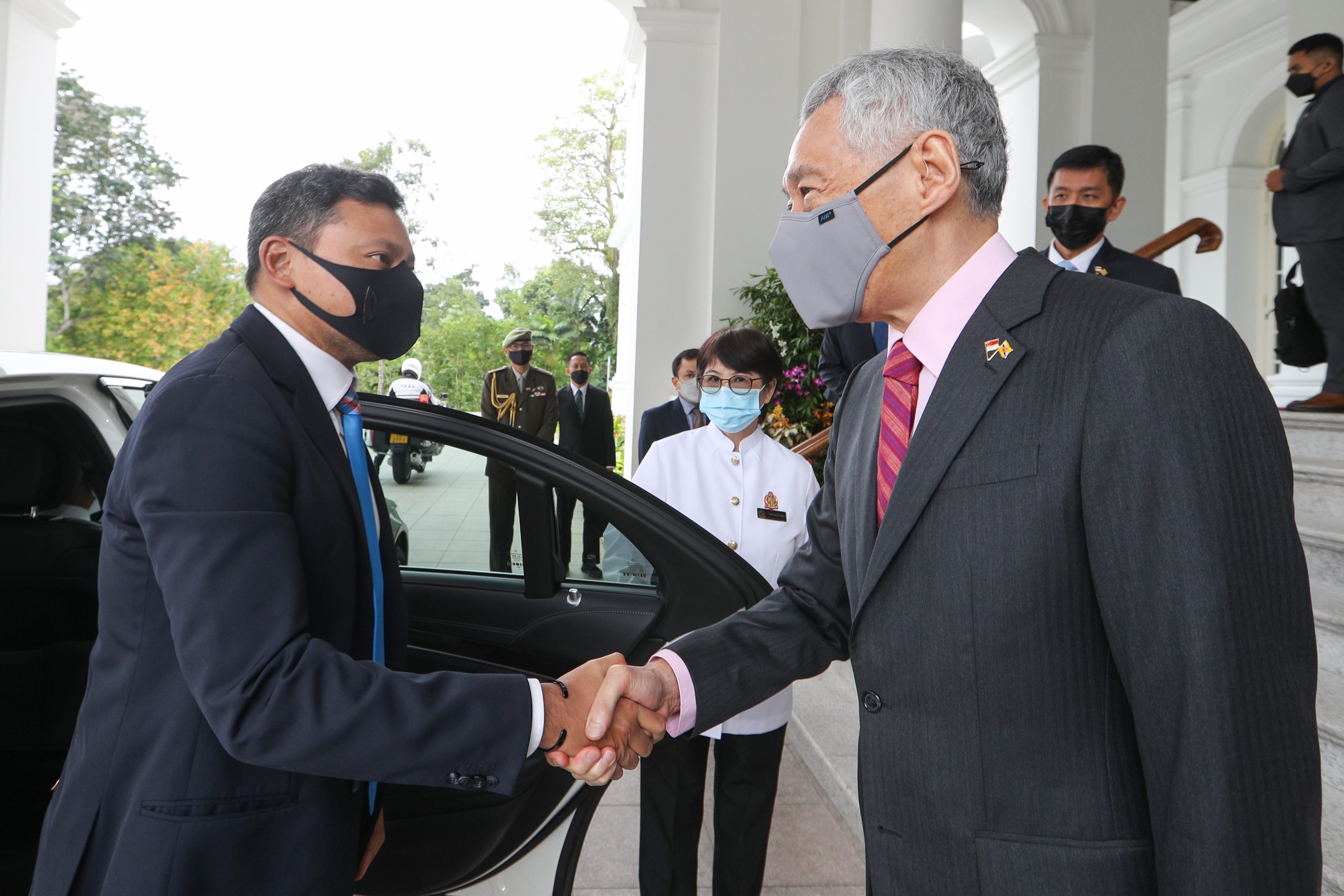 Two masked men in suits shaking hands outside of a white building.