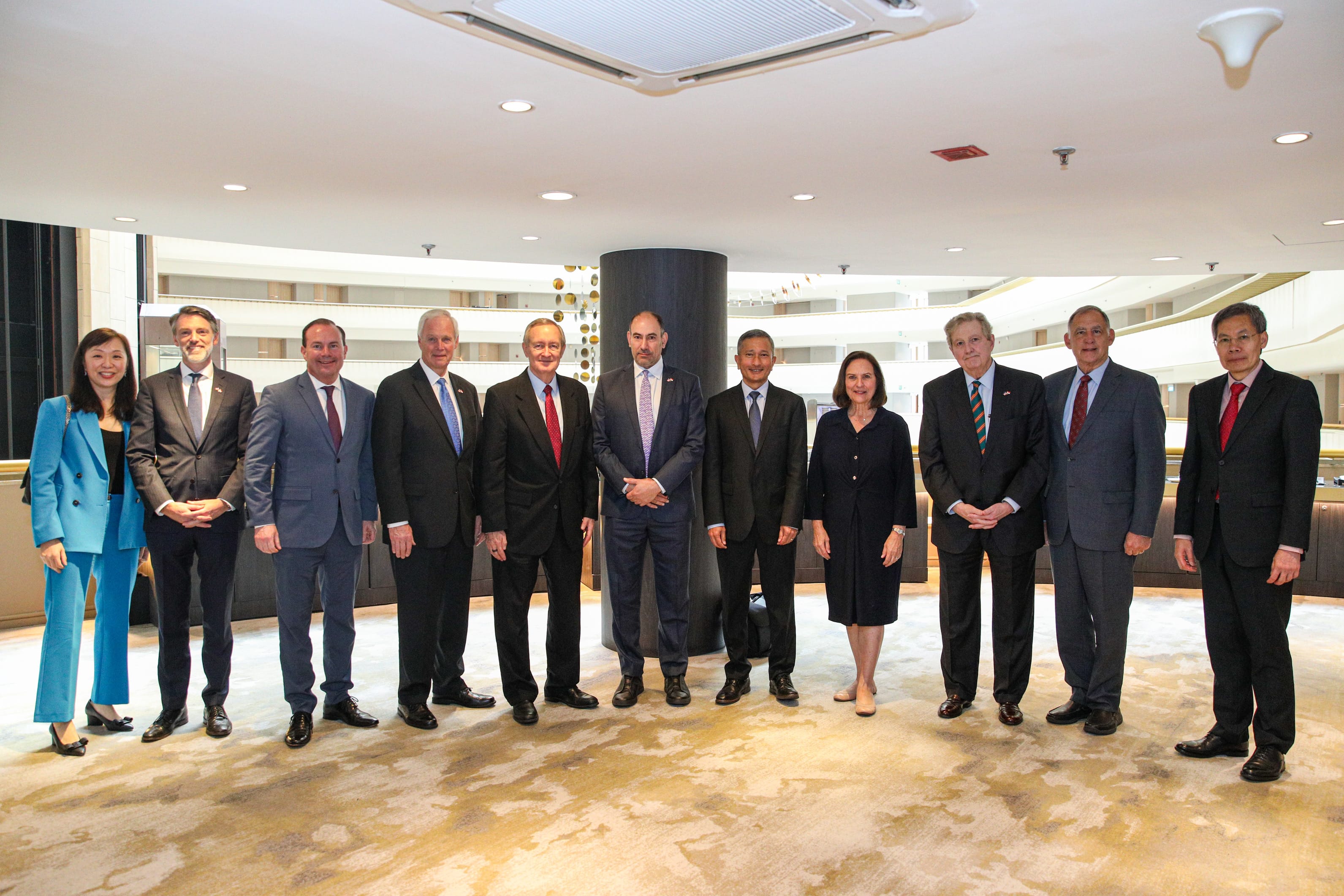 Eleven people in business attire stand in a row indoors.
