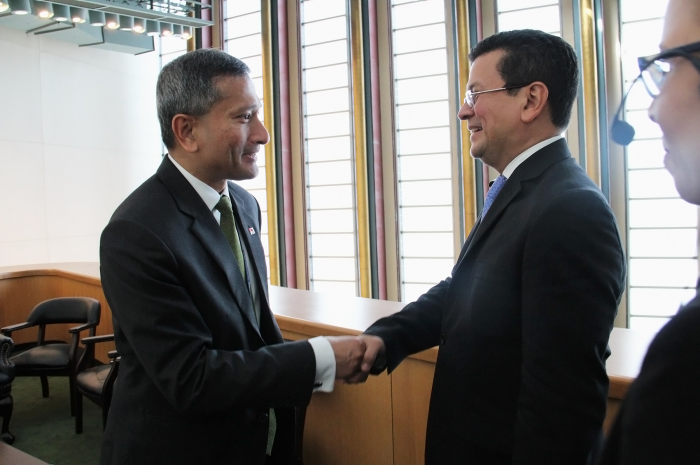 Two men in suits shaking hands indoors, next to a multi-paned window.