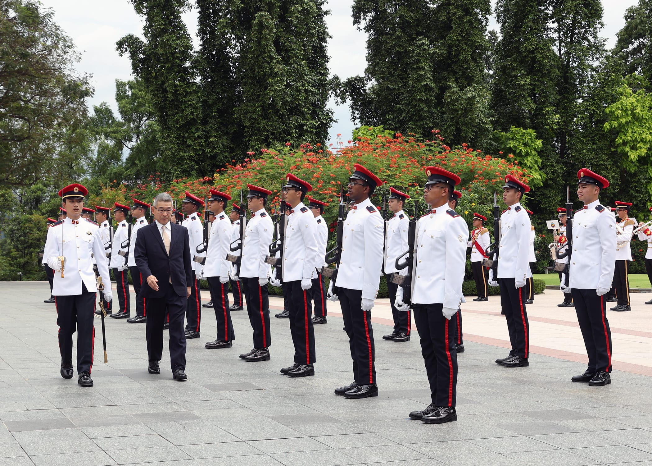 Man in a suit walks past a line of guards in white uniforms with red hats and accents.