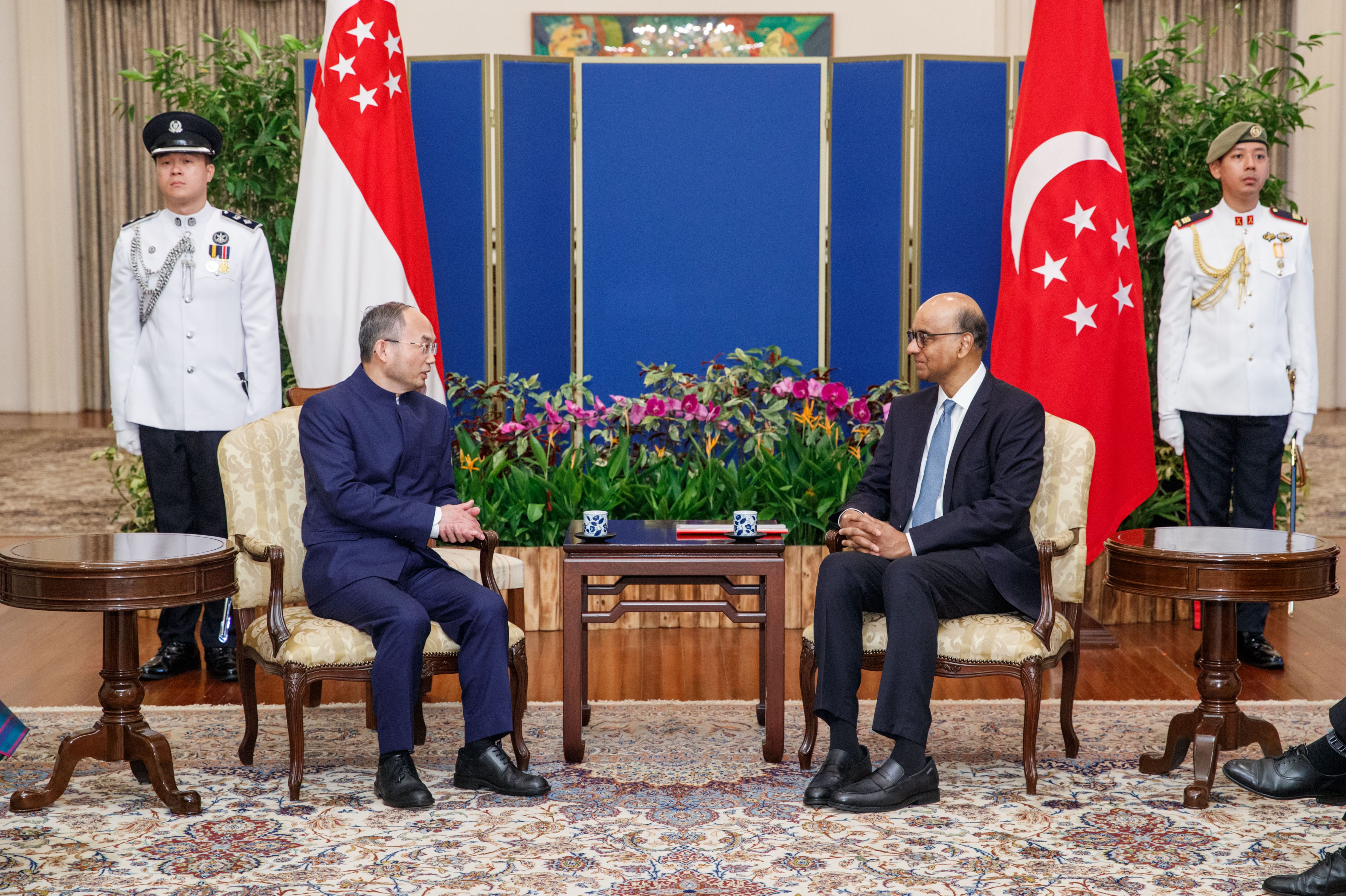 Two men in suits seated, facing each other, flags of Singapore behind them with guards.