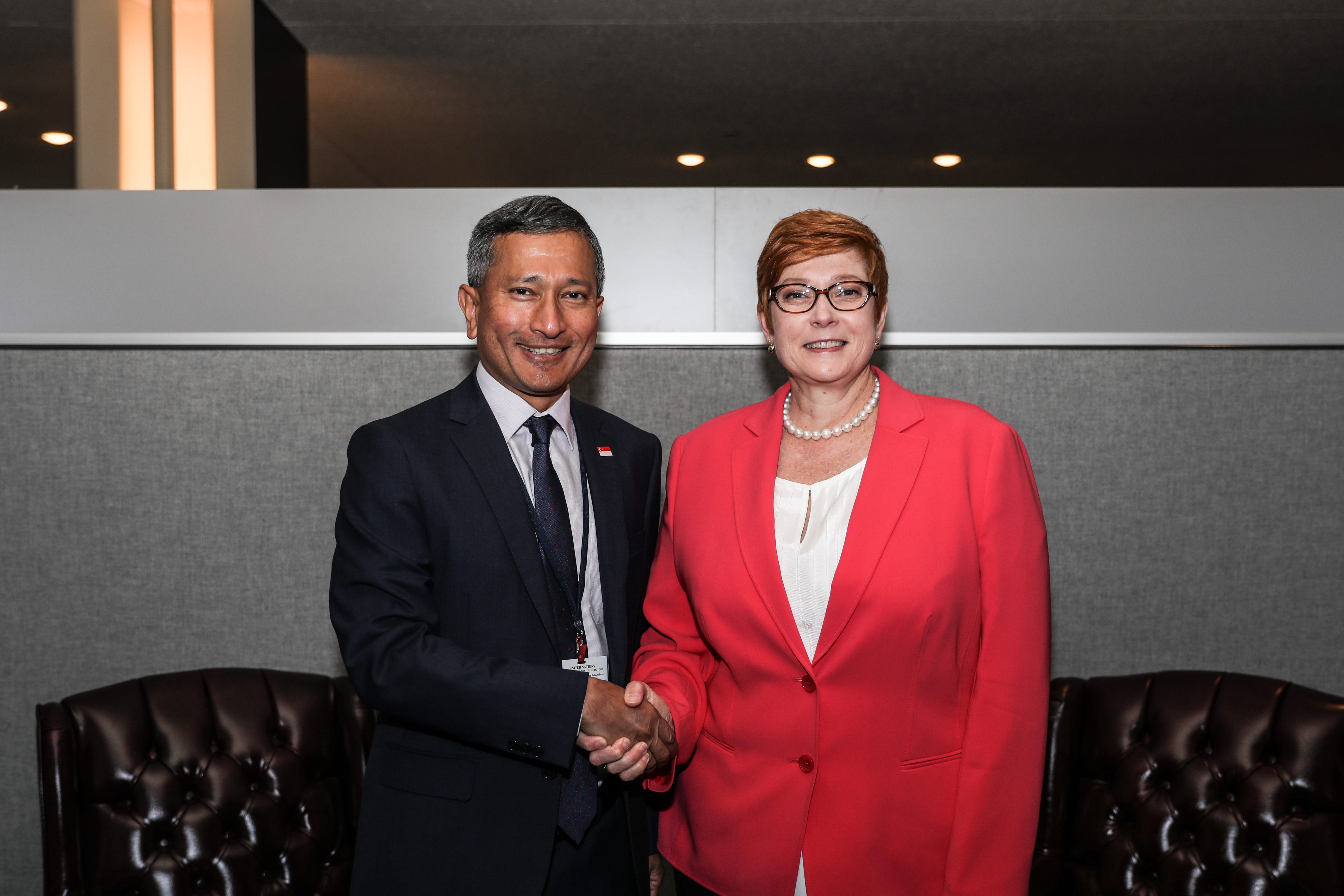Man and woman in suits shaking hands in front of a textured wall.