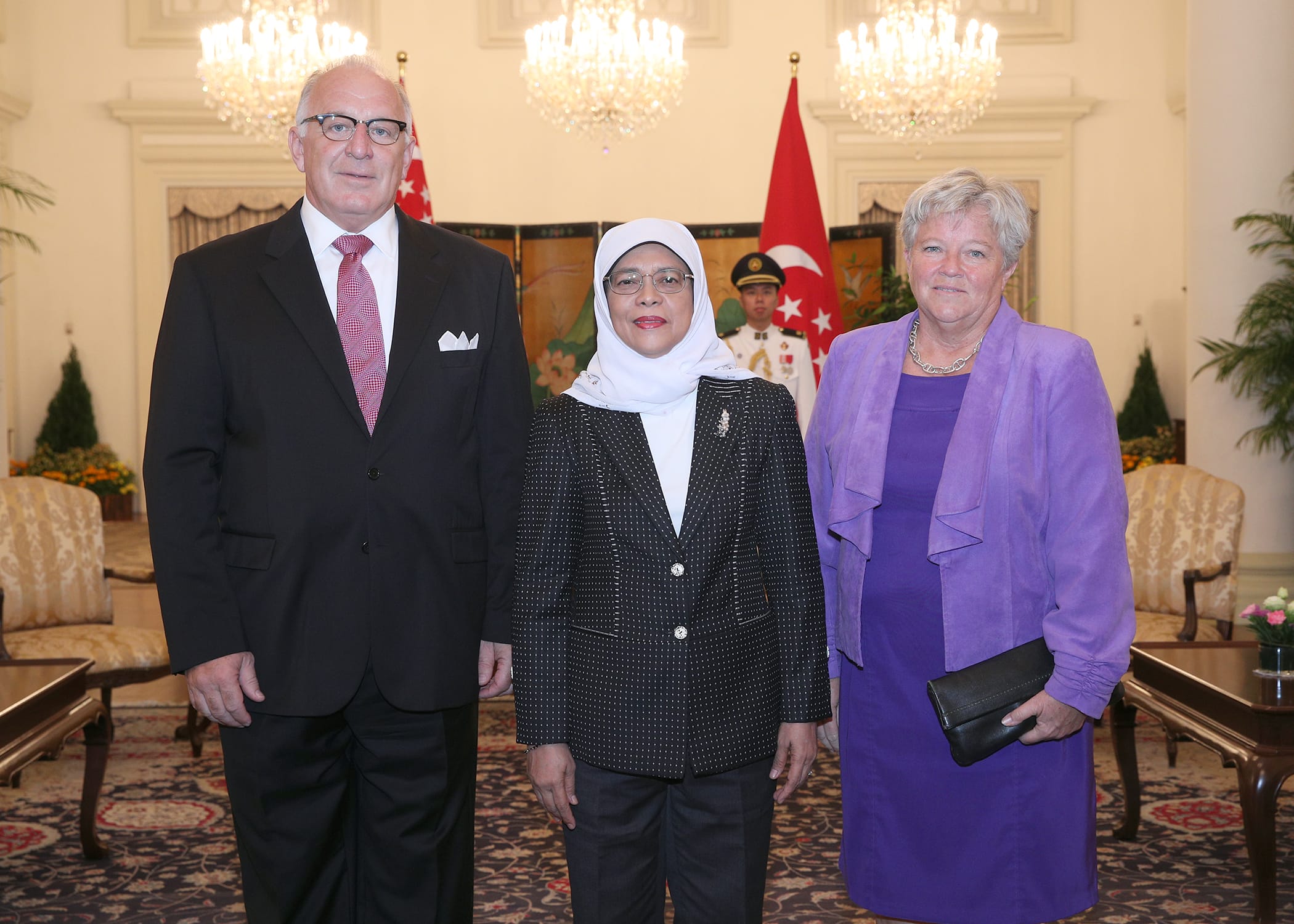 Three people stand indoors, with a Singapore flag in the background.