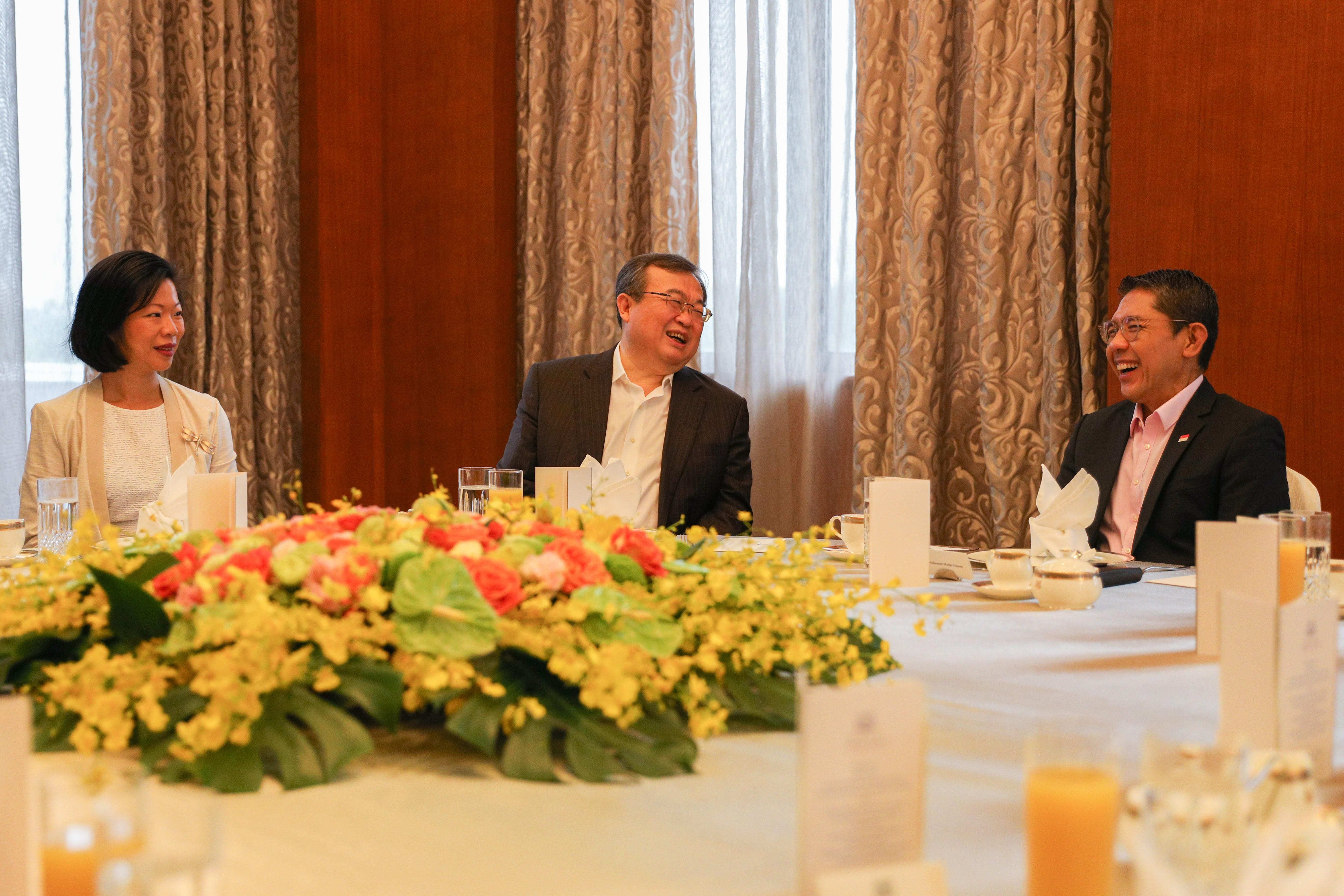 Three people seated at a banquet table with floral centerpiece, laughing.