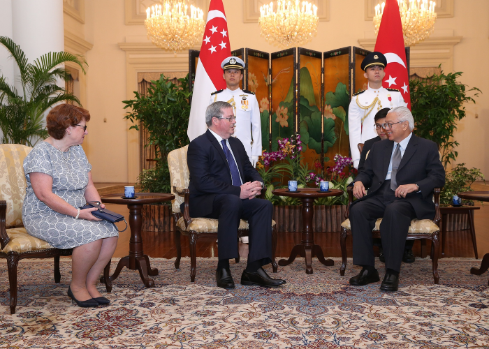 People seated in ornate room with Singapore flags and honor guard behind them.