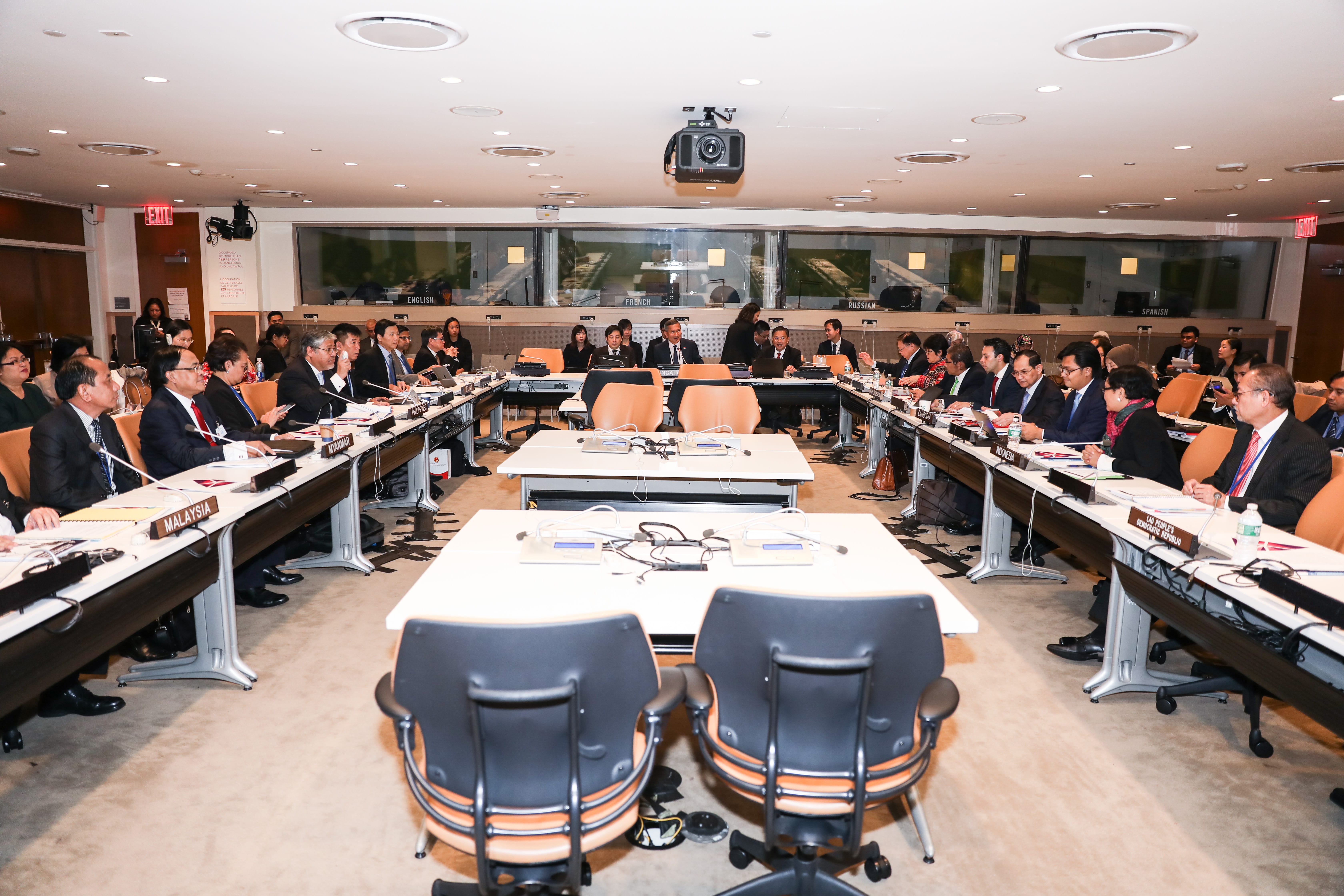 U-shaped conference table with country placards and attendees. Translation booths visible.