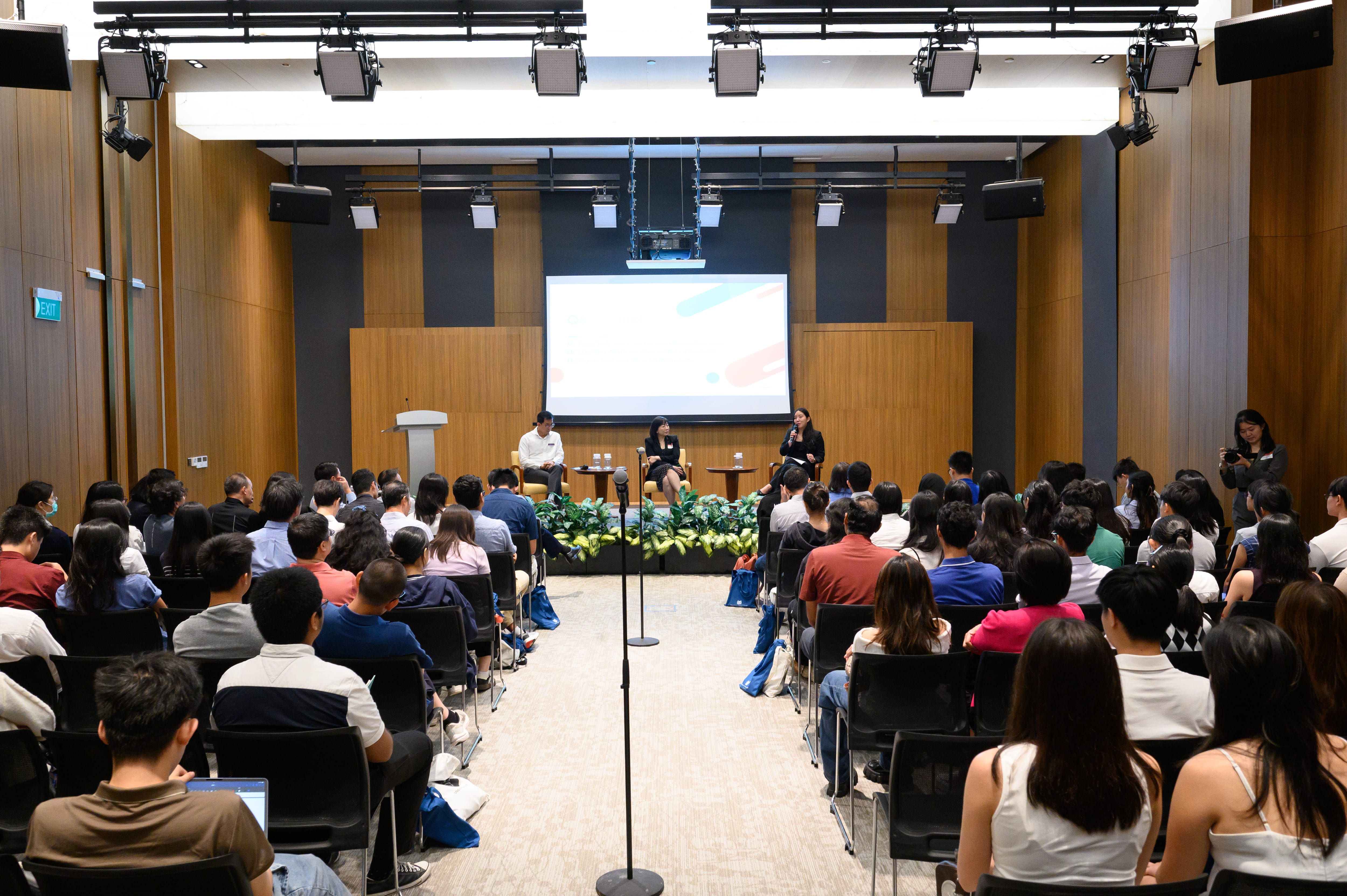 Audience seated for a panel discussion with three speakers on stage