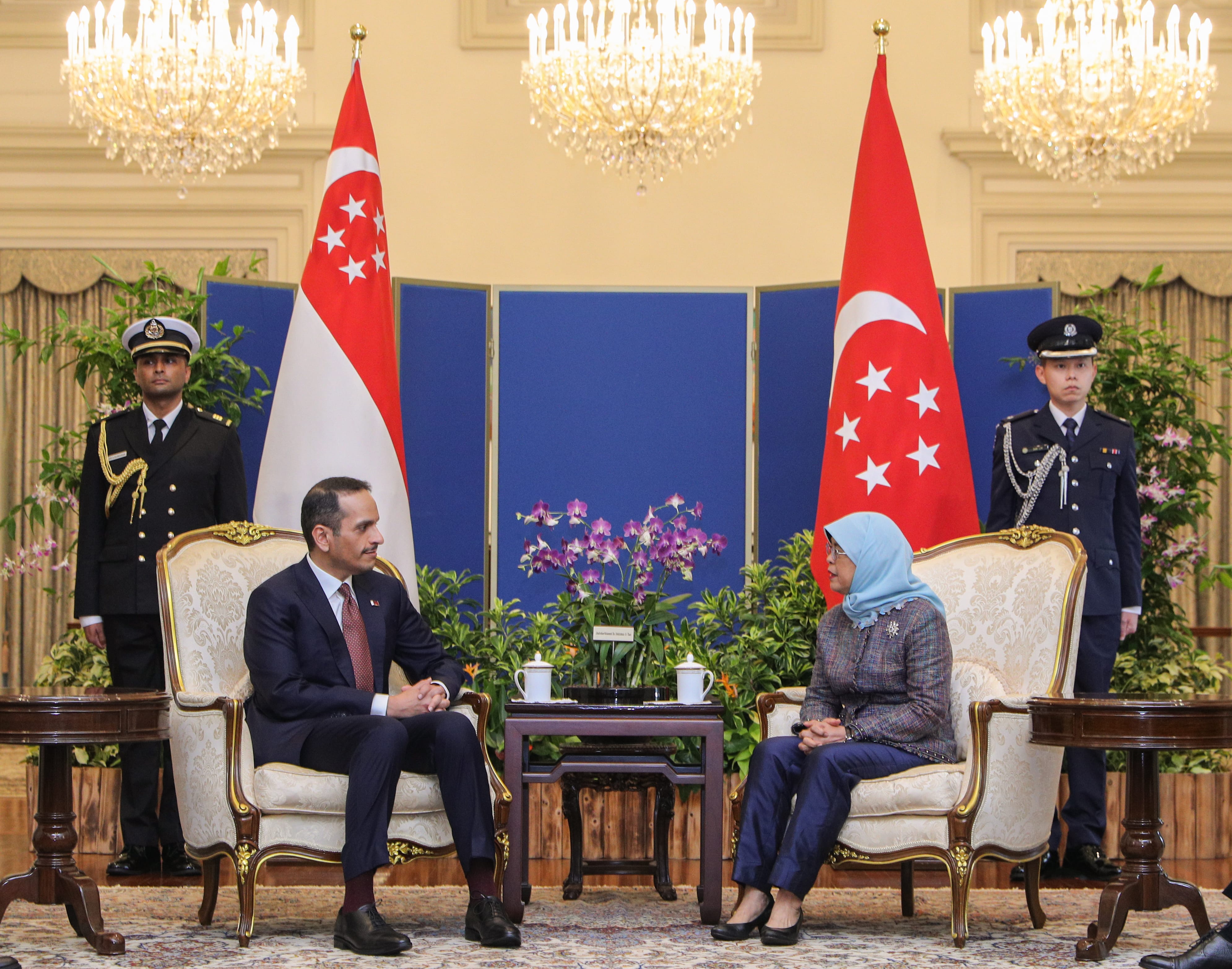 Man and woman seated facing each other with Singapore and Turkey flags. Guards stand behind.