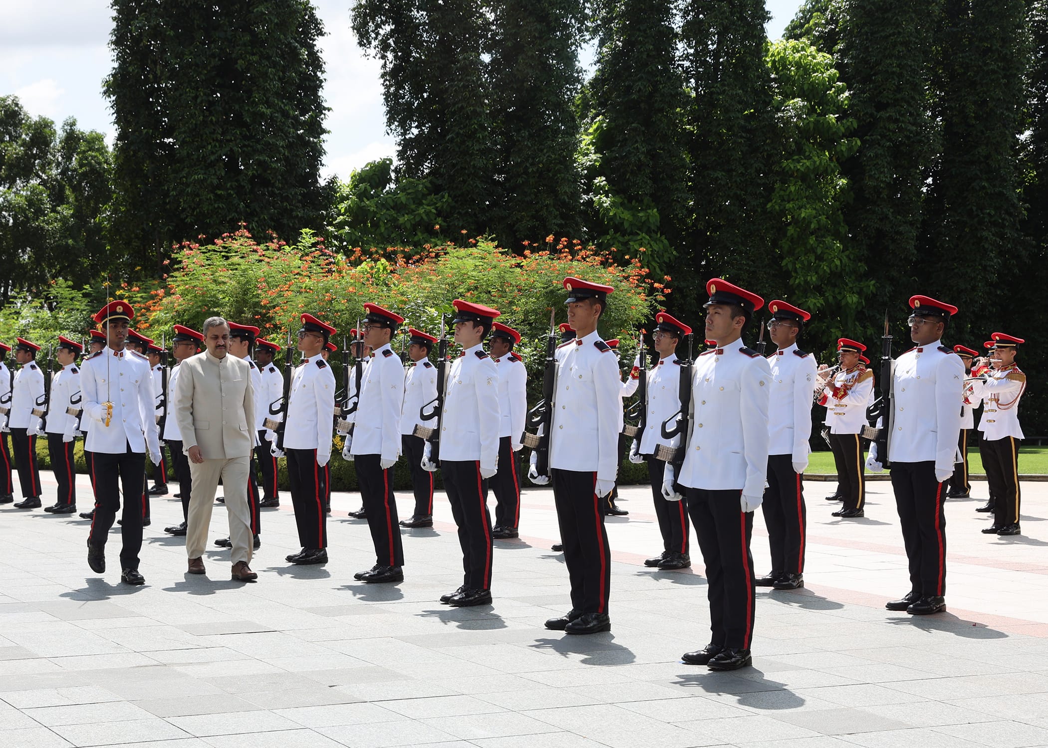 Military honor guard in white uniforms and red hats stands in formation for a dignitary.
