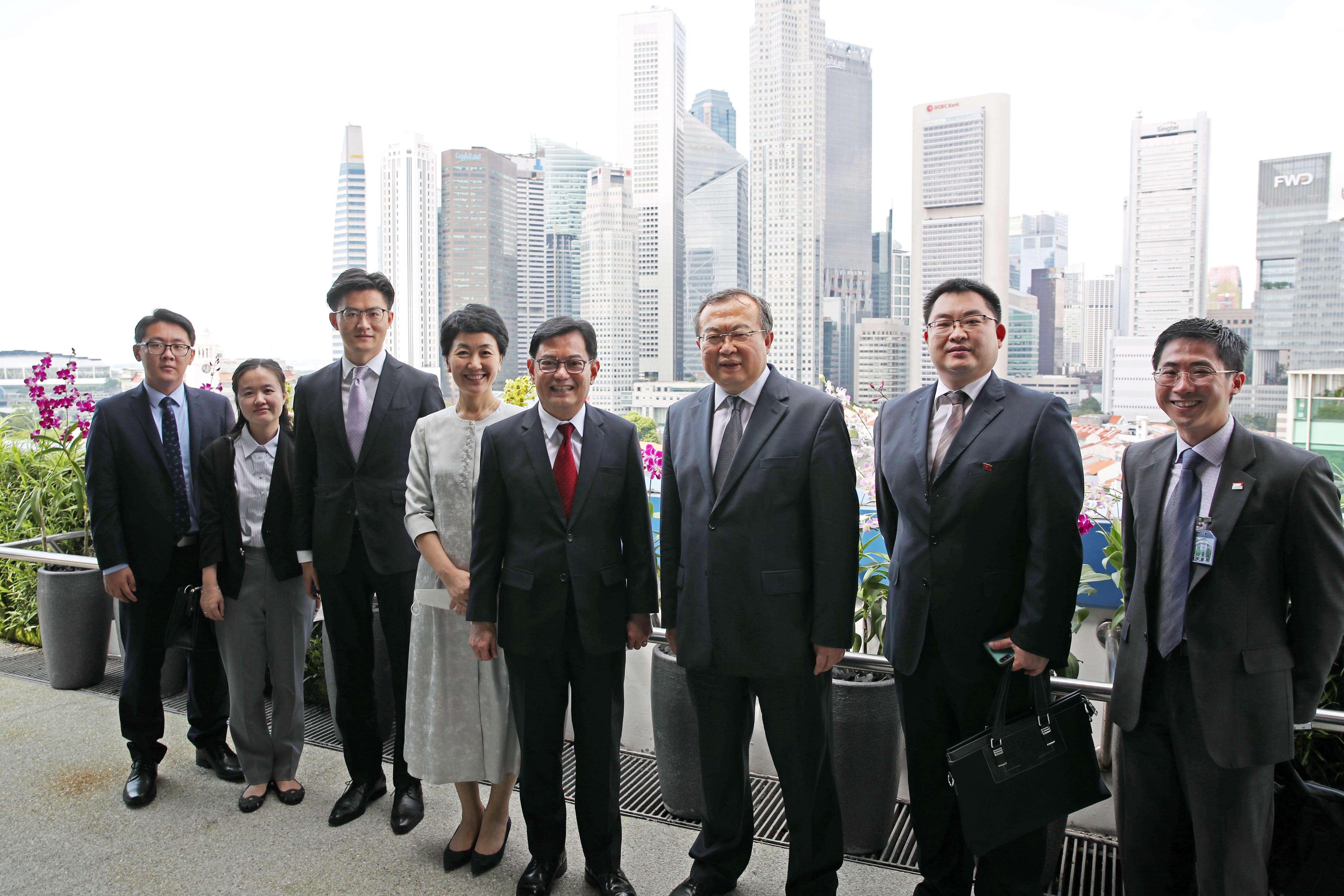 Eight people in suits pose, Singapore skyline behind them.