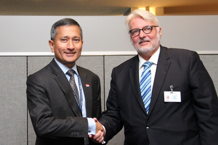 Two men in suits shaking hands, one with an Indonesian flag pin.