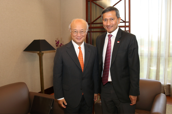 Two men in suits, one with a Singapore flag pin, stand in a room with armchairs.