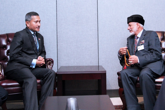 Two men in suits seated and talking, one holding prayer beads.