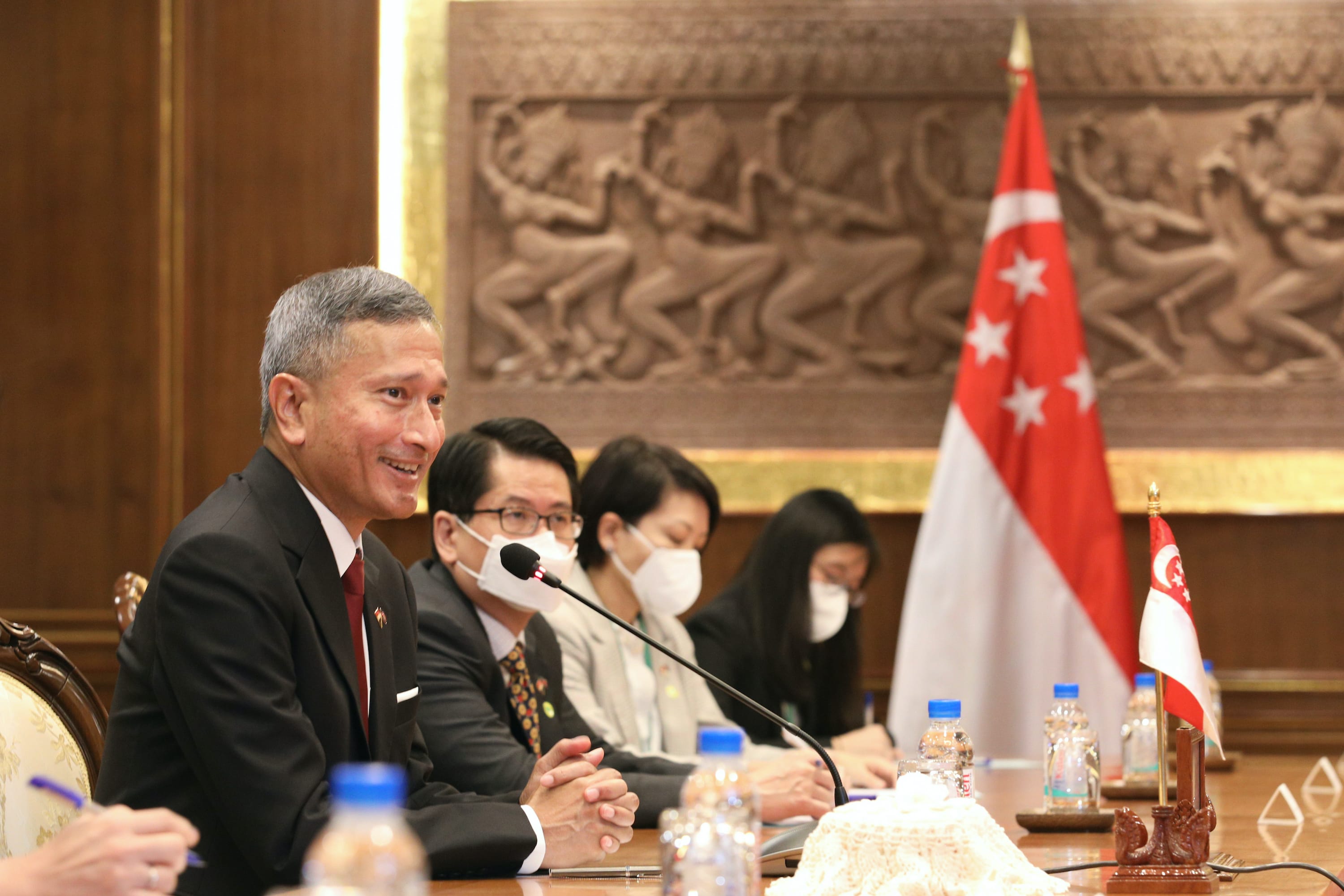 People at a table with microphones and bottled water, and Singapore flags displayed.