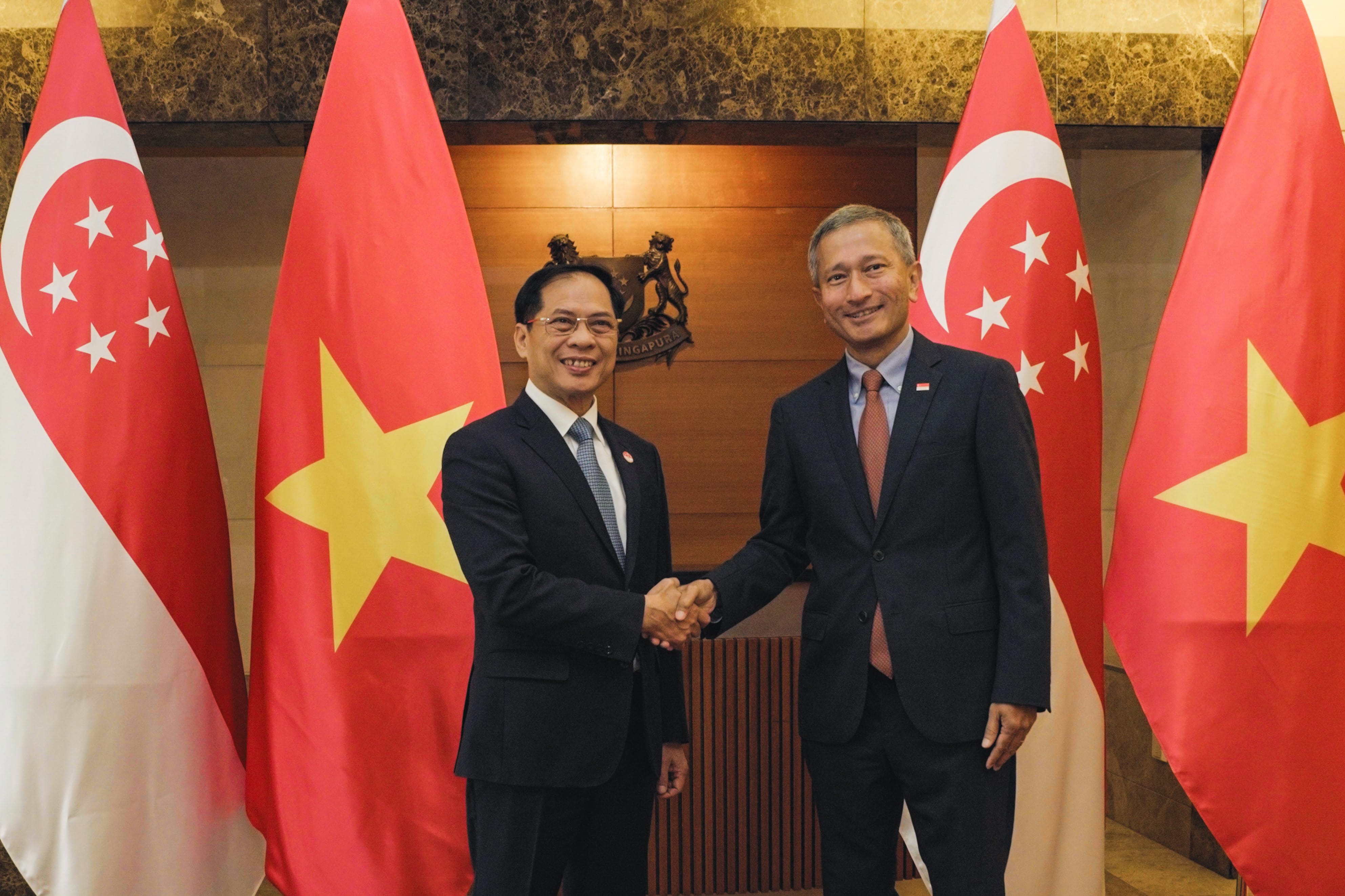 Two men in suits shake hands, flanked by Singapore and Vietnam flags, with Singapore crest in background.