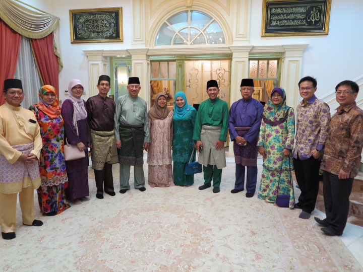 Group of eleven people posed indoors, some in traditional Malay dress.
