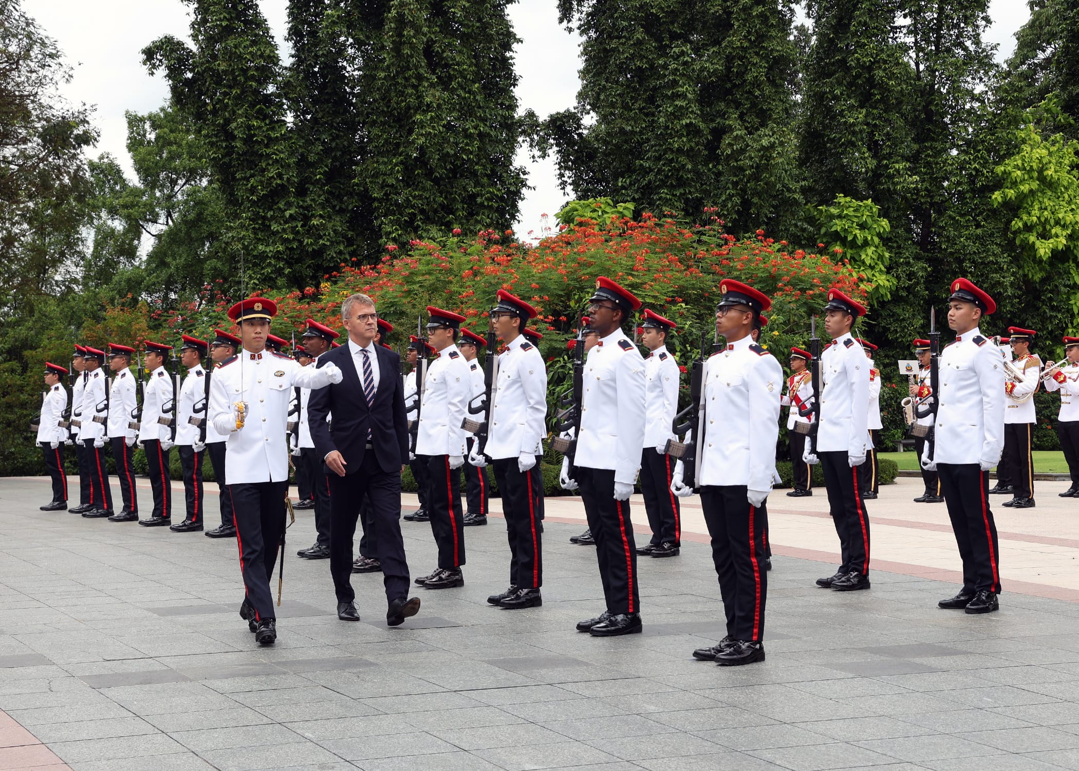 Military personnel in white uniforms with red accents, led by a man in a suit.