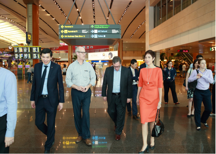 Group of people walking in Changi Airport, under directional signs.