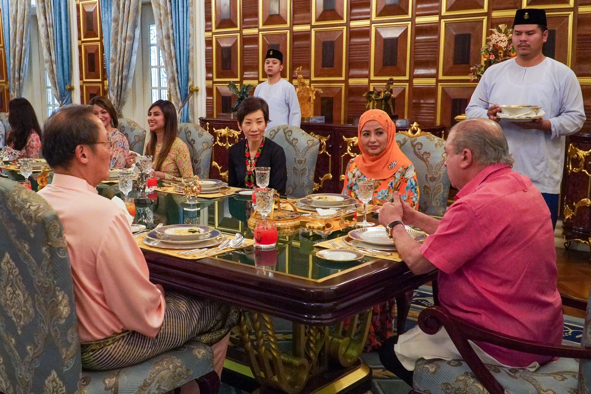 People seated at a long dining table with servers in a formal dining room.