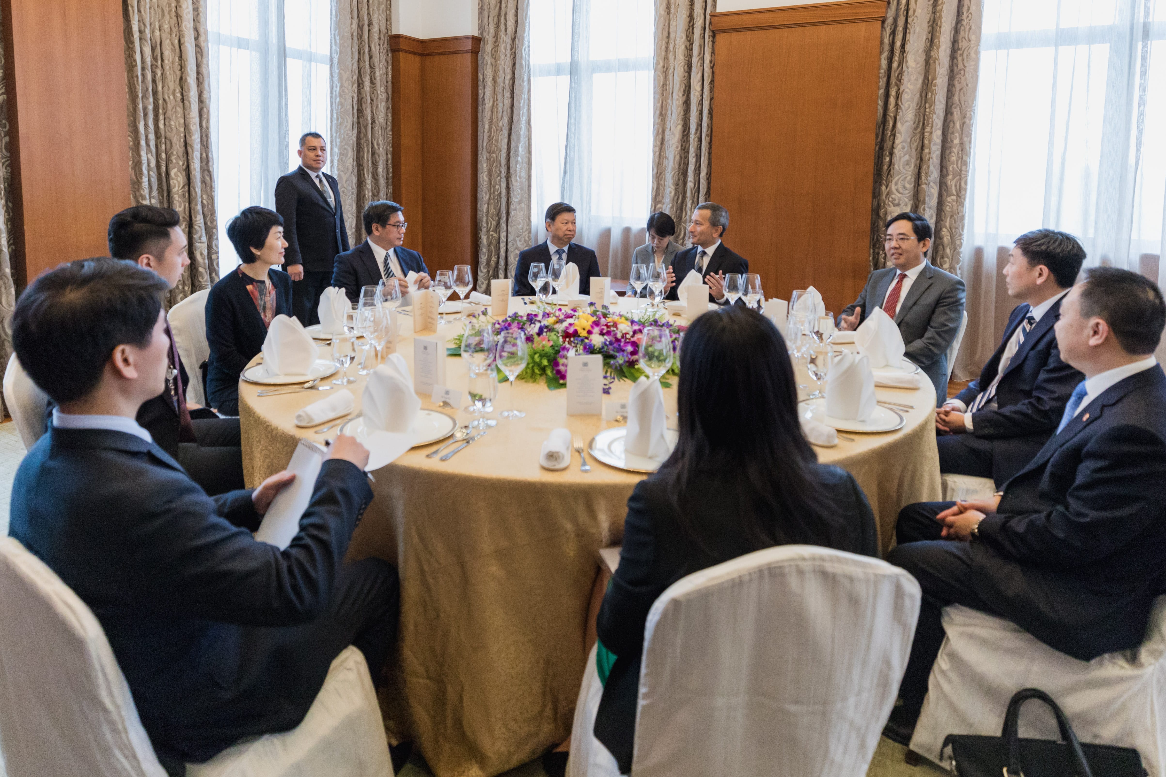 People in business attire sit around a round table in a meeting room.