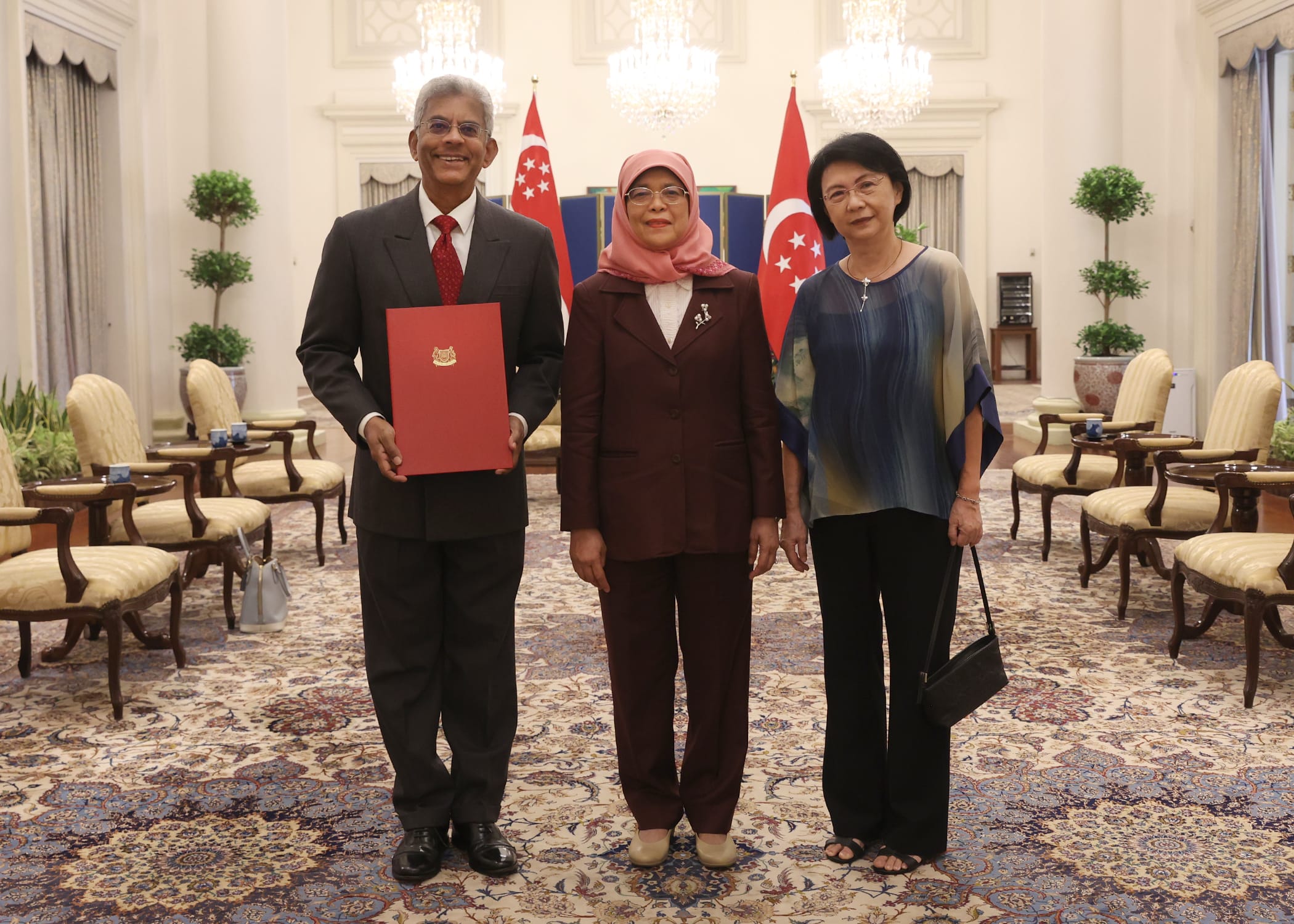 President Halimah Yacob of Singapore poses with two people indoors, Singapore flags behind them.