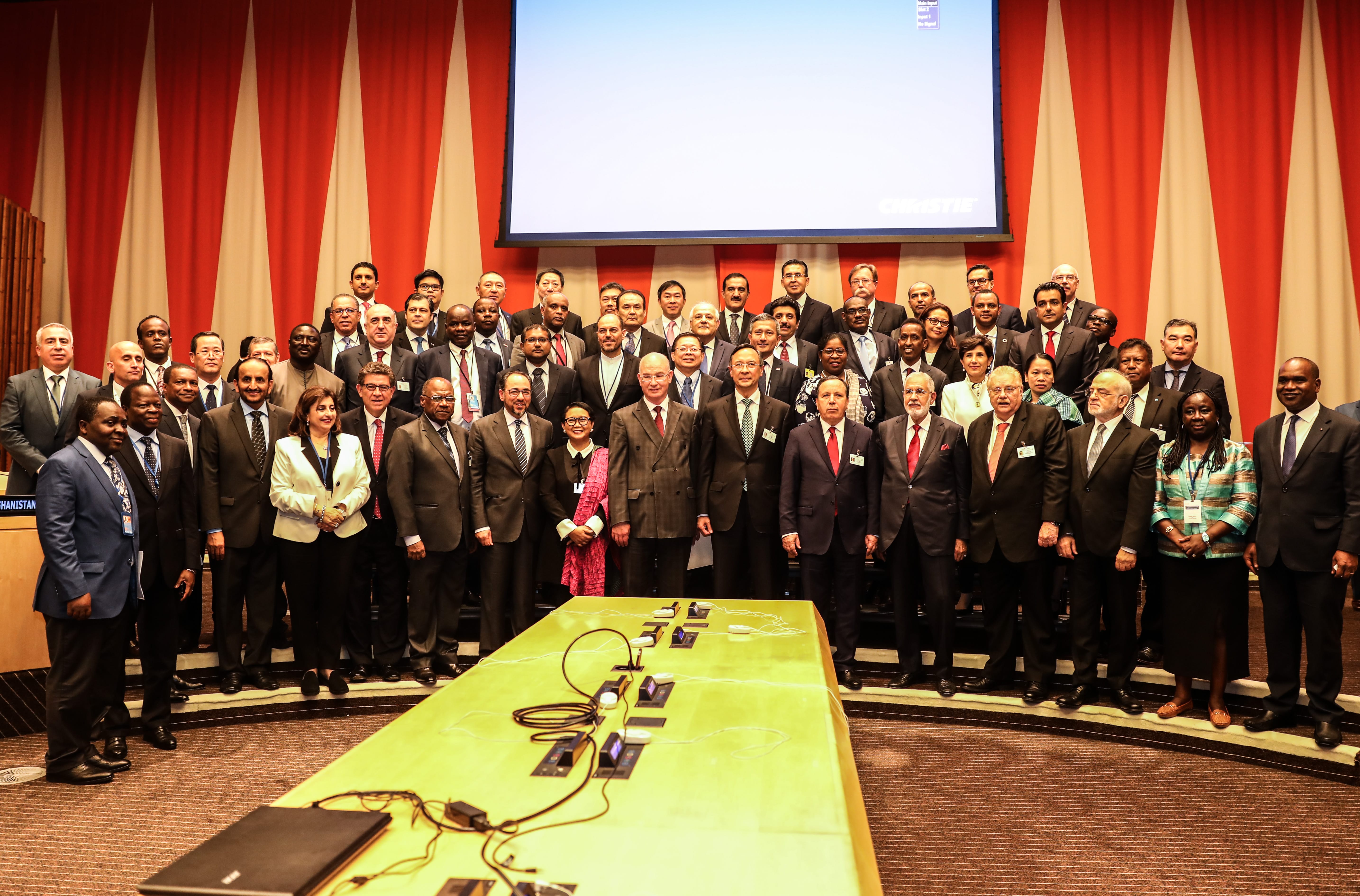 Group poses before Christie-branded screen in front of red/white striped wall. Table with microphone/headphone sets.