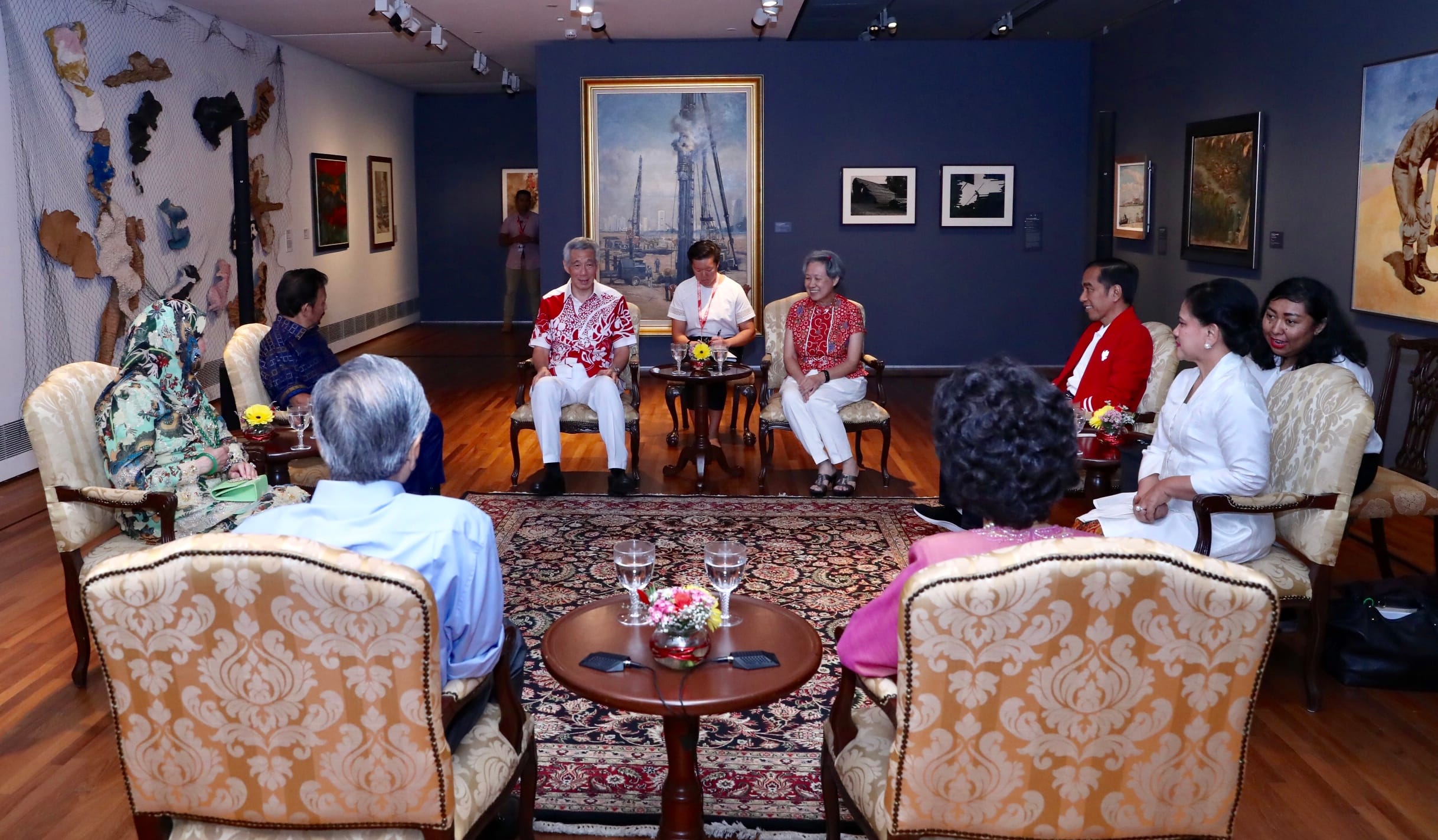 Group of people sitting in an art gallery with paintings on the wall.