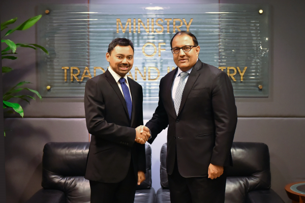 Two men in suits shaking hands in front of "Ministry of Trade and Industry" sign.