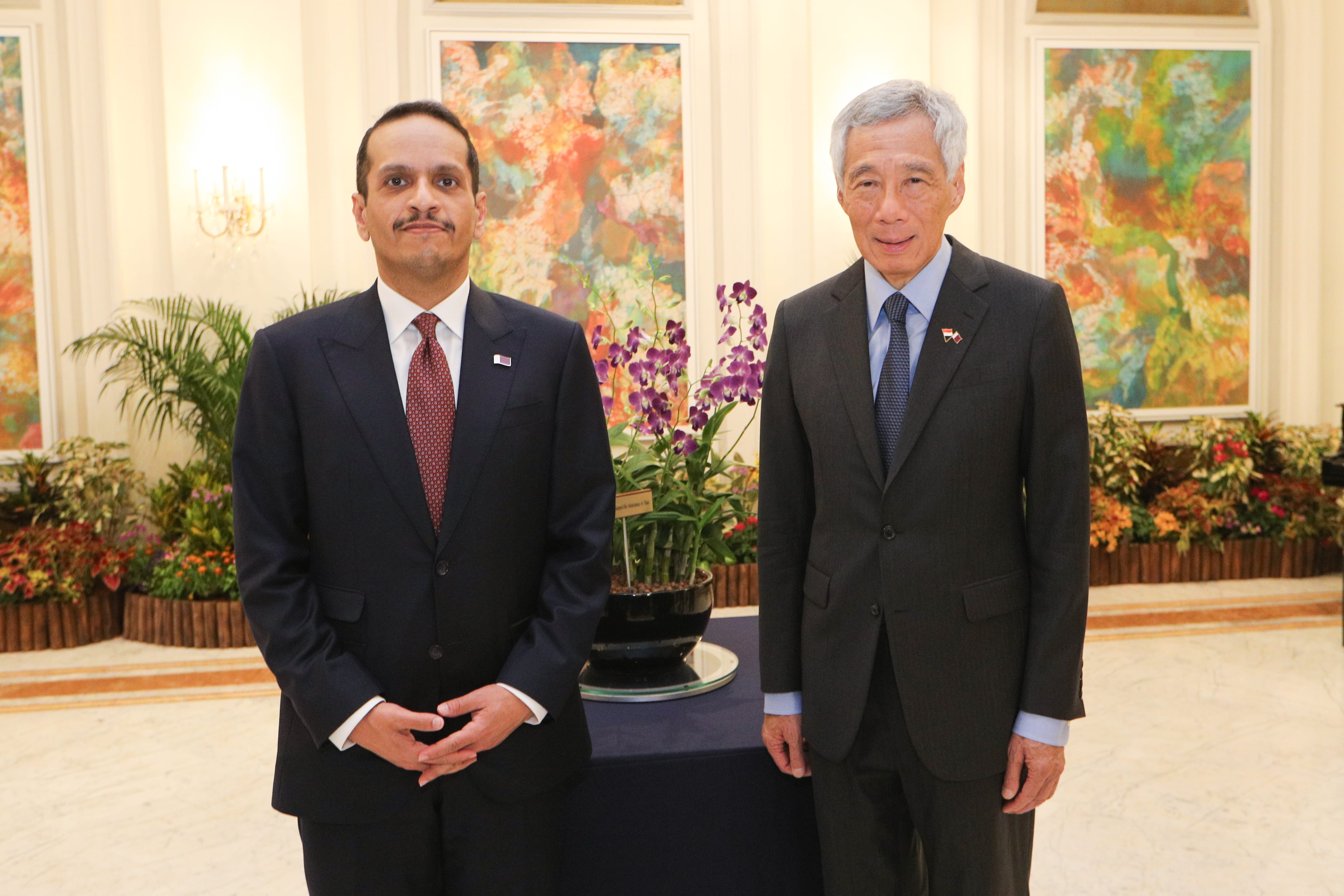 Two men in suits sit across from each other with a table between them.