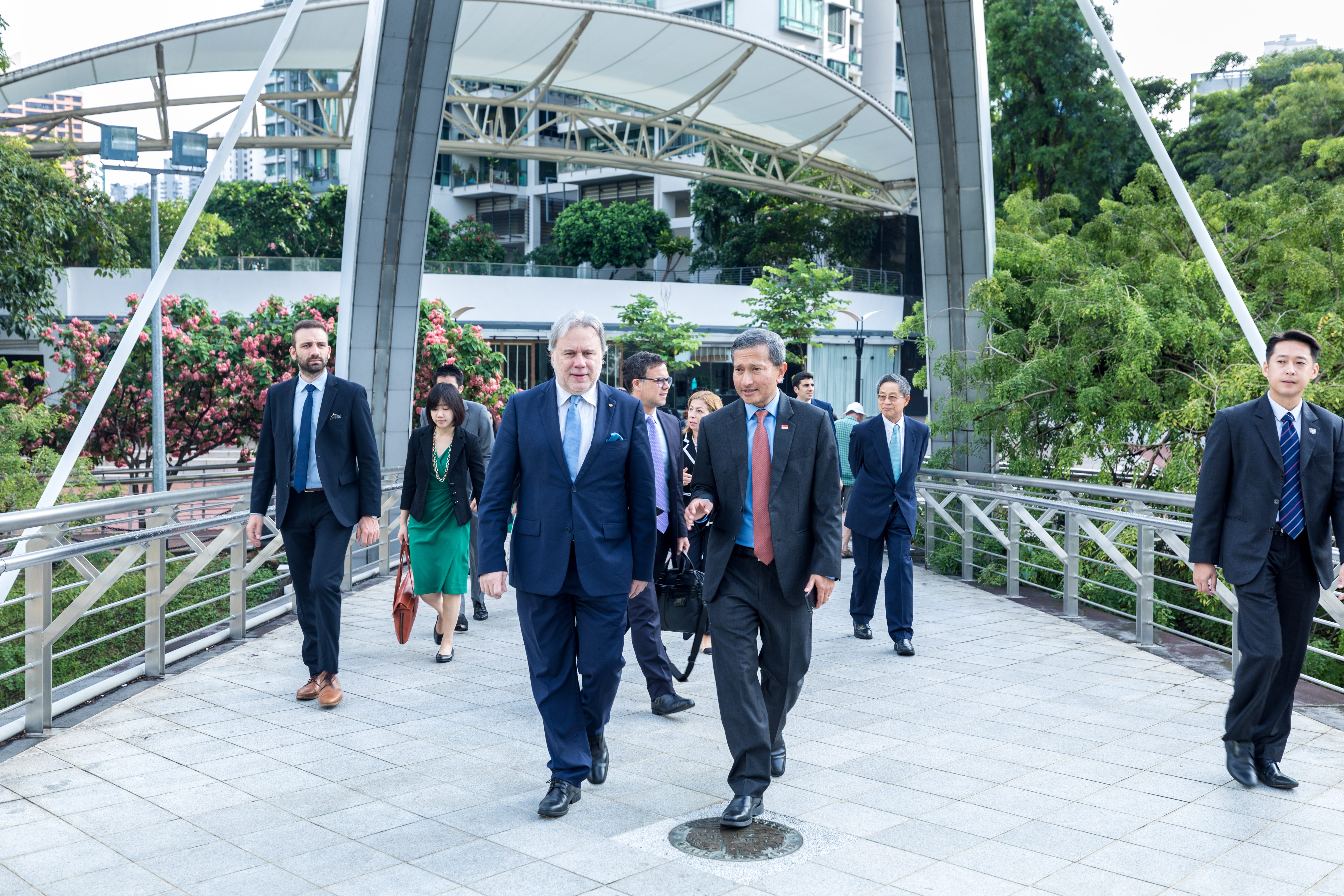 Three men in suits pose before flags and a "Global Coalition to Defeat ISIS" sign. One wears traditional Arab dress.