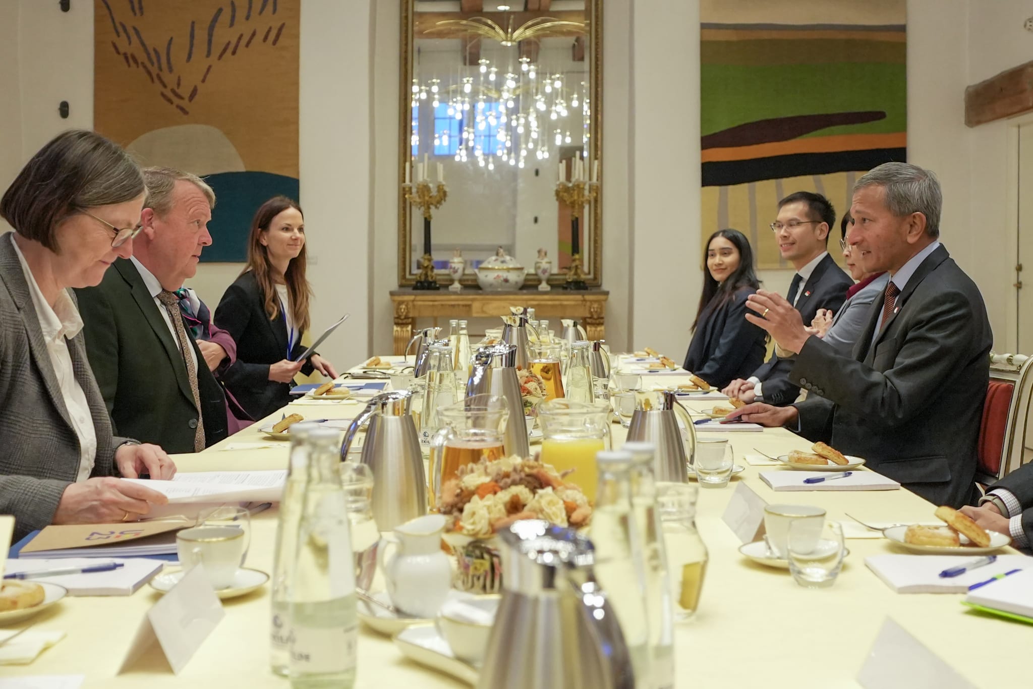 Group of people sitting around a long conference table with beverages and papers.