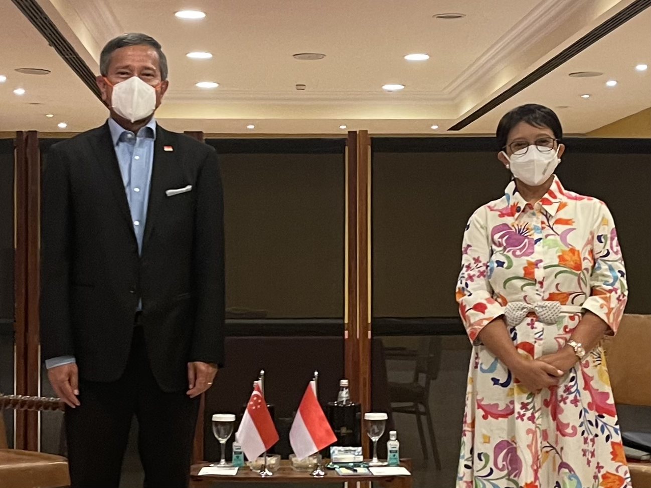 Two masked individuals stand near Singapore and Indonesia flags.