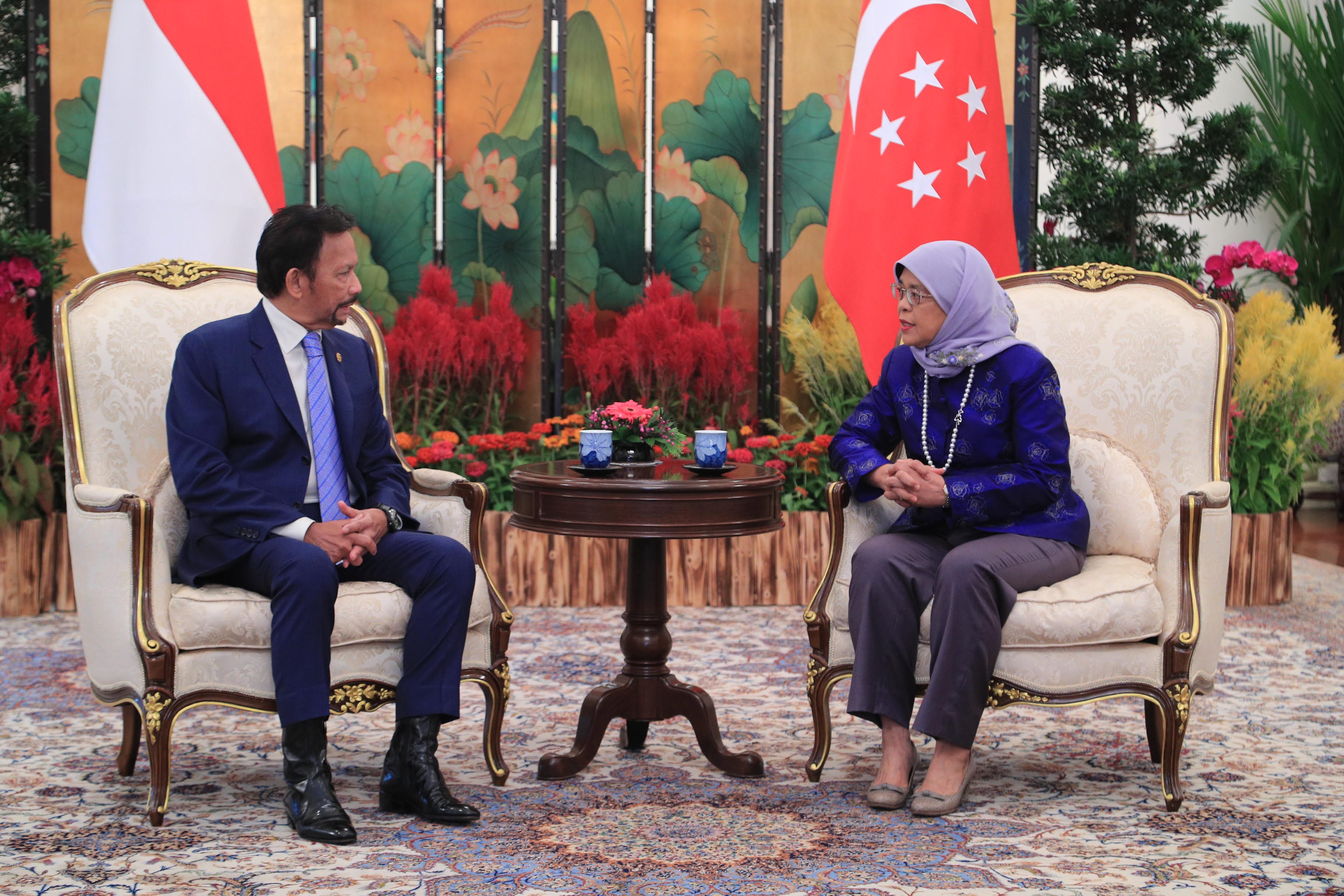 Group of people posed on a red carpeted staircase with white railing, with floral arrangements.