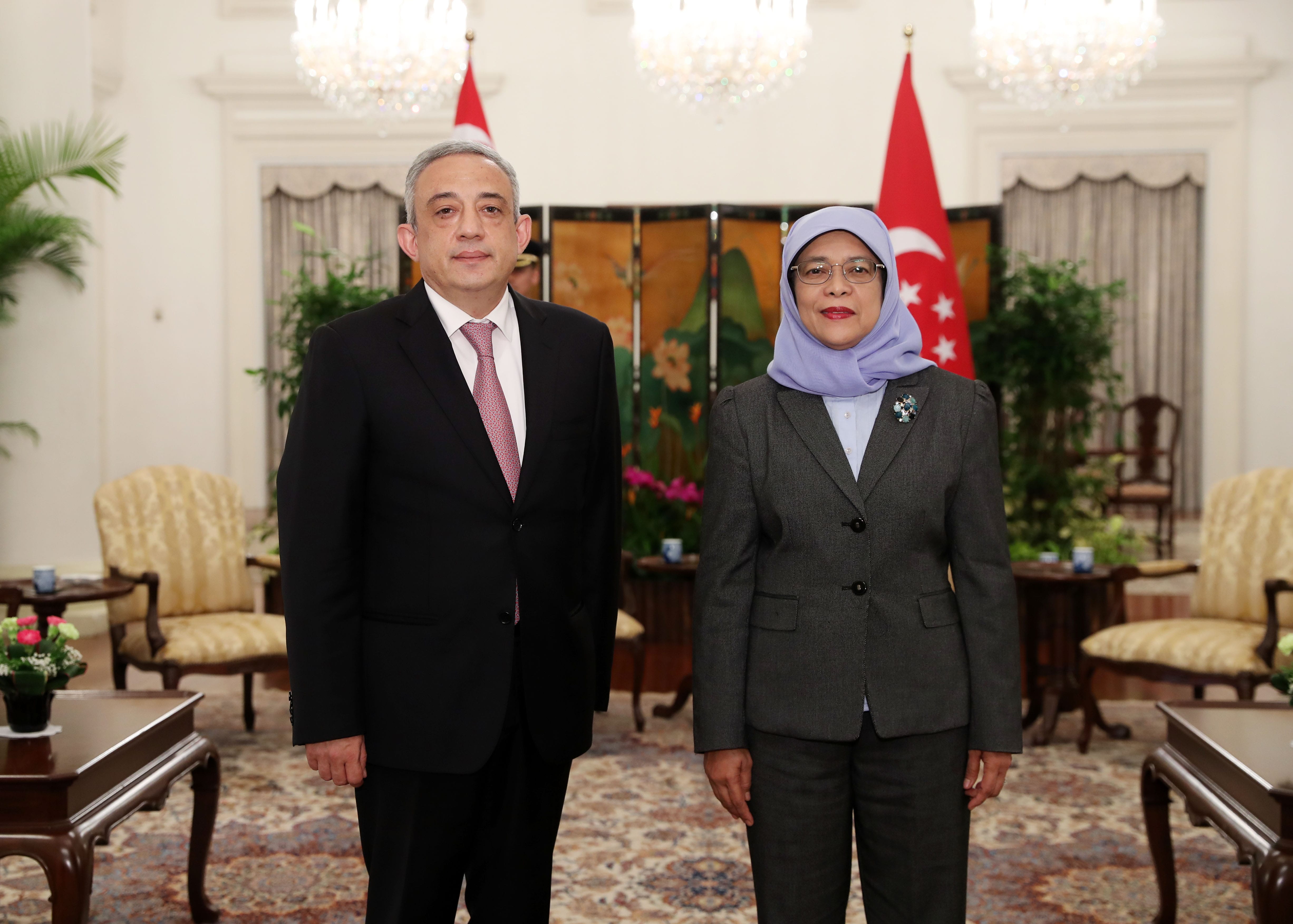 Man and Halimah Yacob in a suit, with Singapore flags in the background.