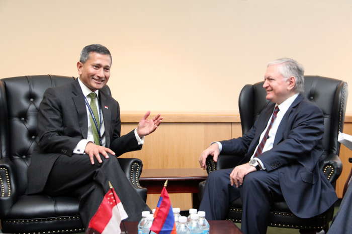 Two men in suits sit in leather chairs, with flags of Singapore and Armenia on a table.