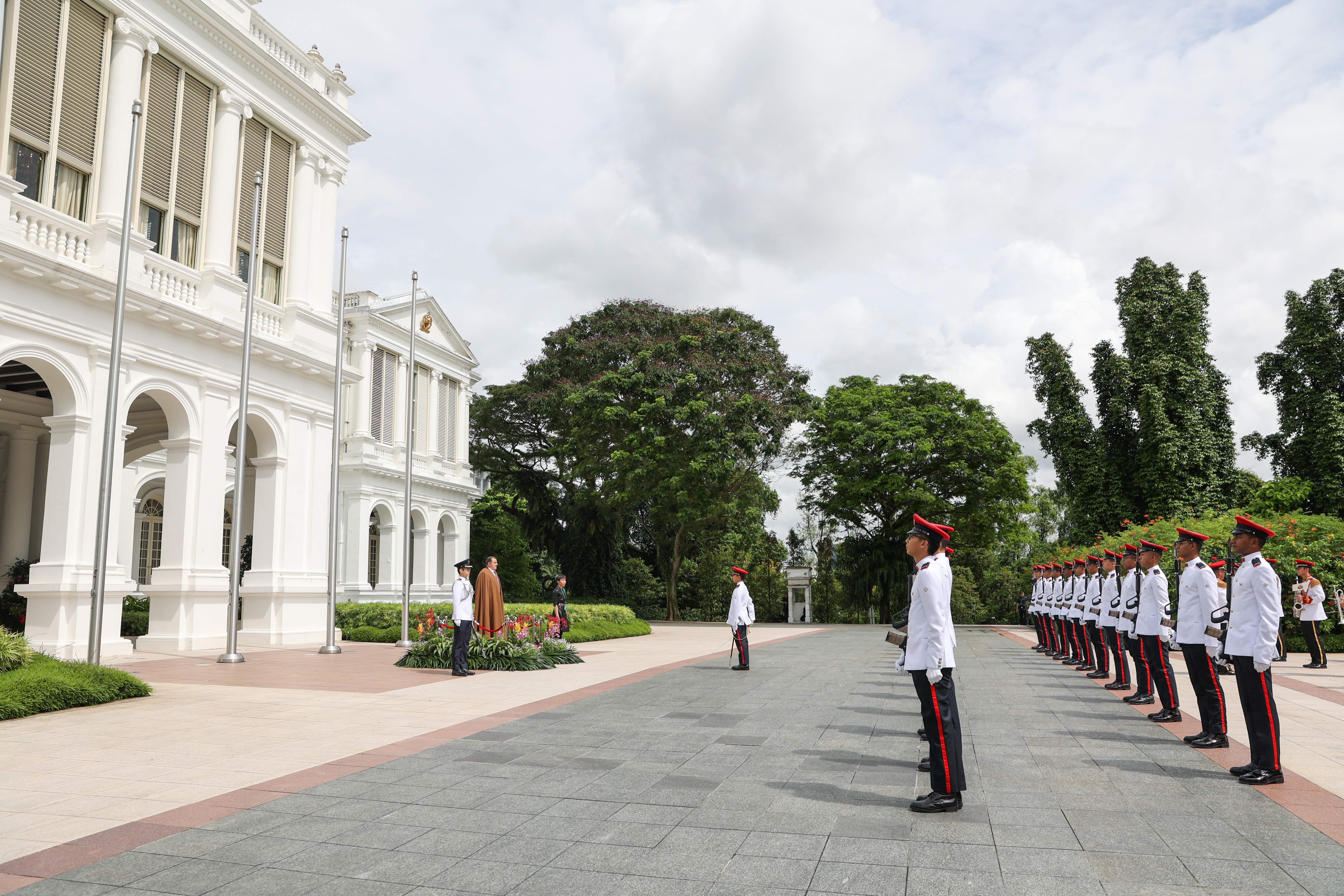 Soldiers in dress uniform stand at attention outside a large white building.