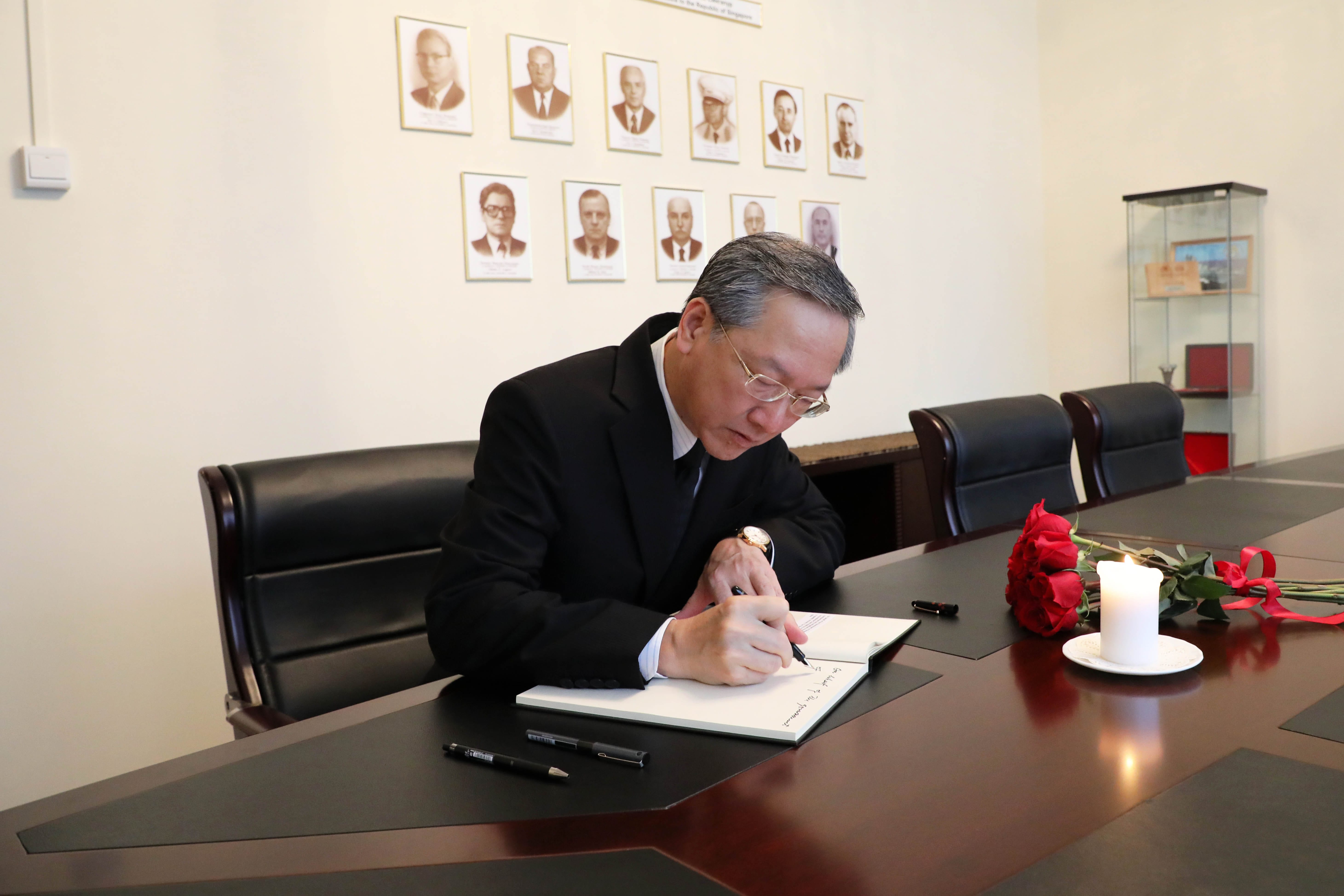 Man writing in a notebook on a dark table with a candle and roses. Portraits on the wall.