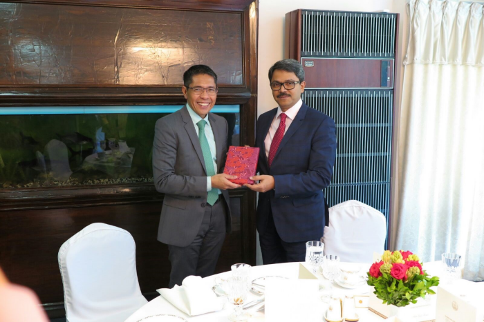 Two men in suits exchange a wrapped gift at a table set for dining.