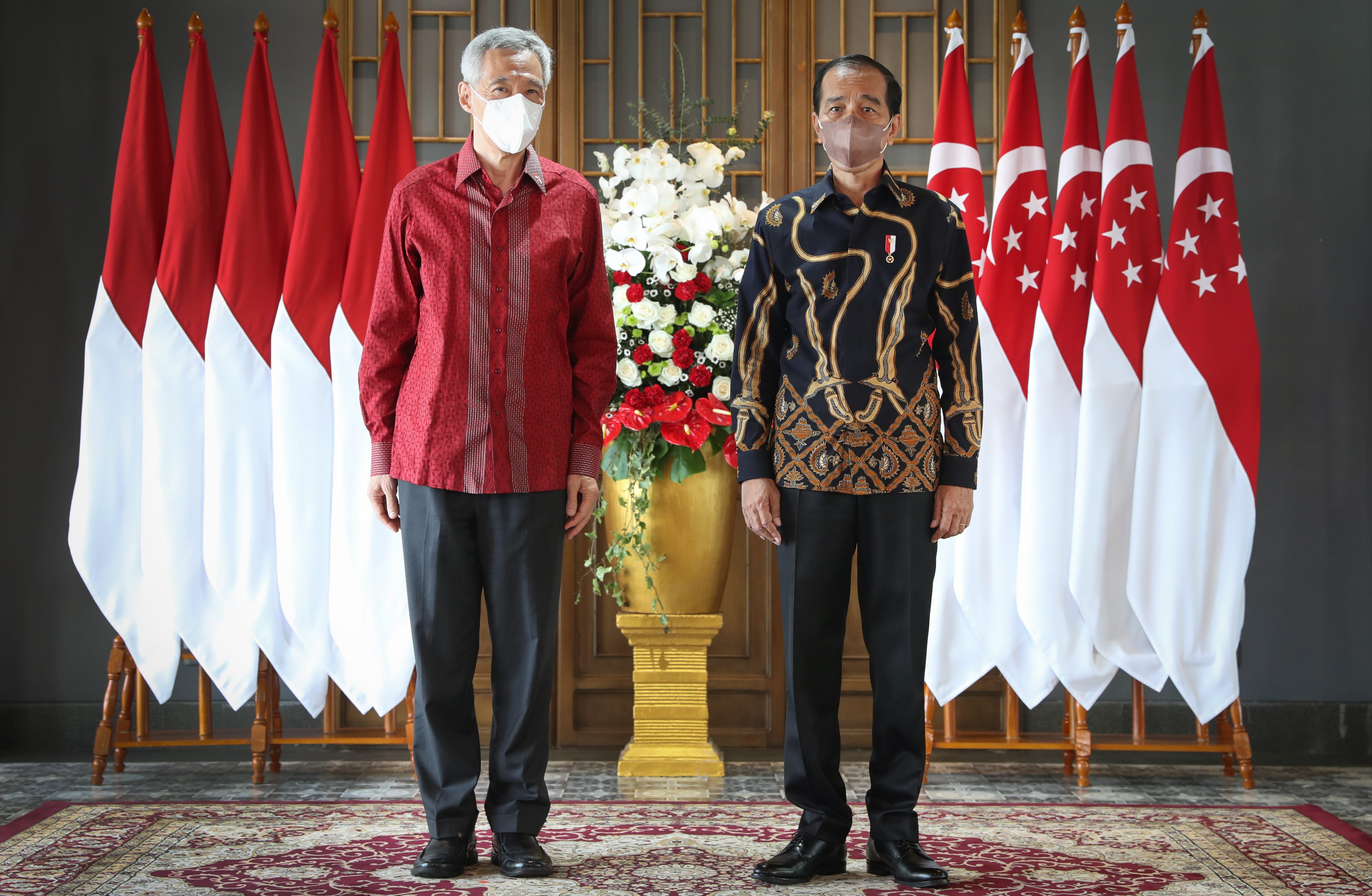 Two men with face masks stand between Indonesian and Singaporean flags.