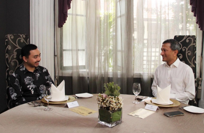 Two men seated at a formal dining table are turned toward each other in conversation.