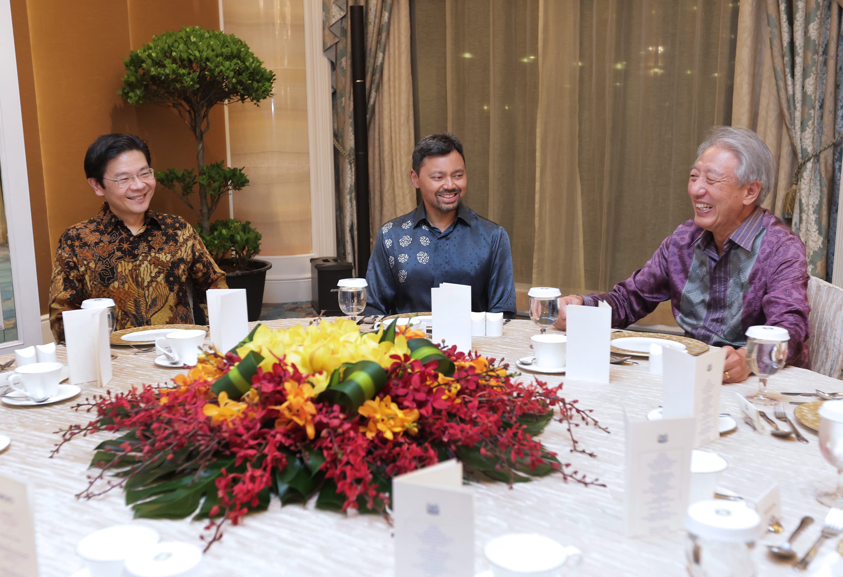 Three men seated at a formal dining table with floral centerpiece.