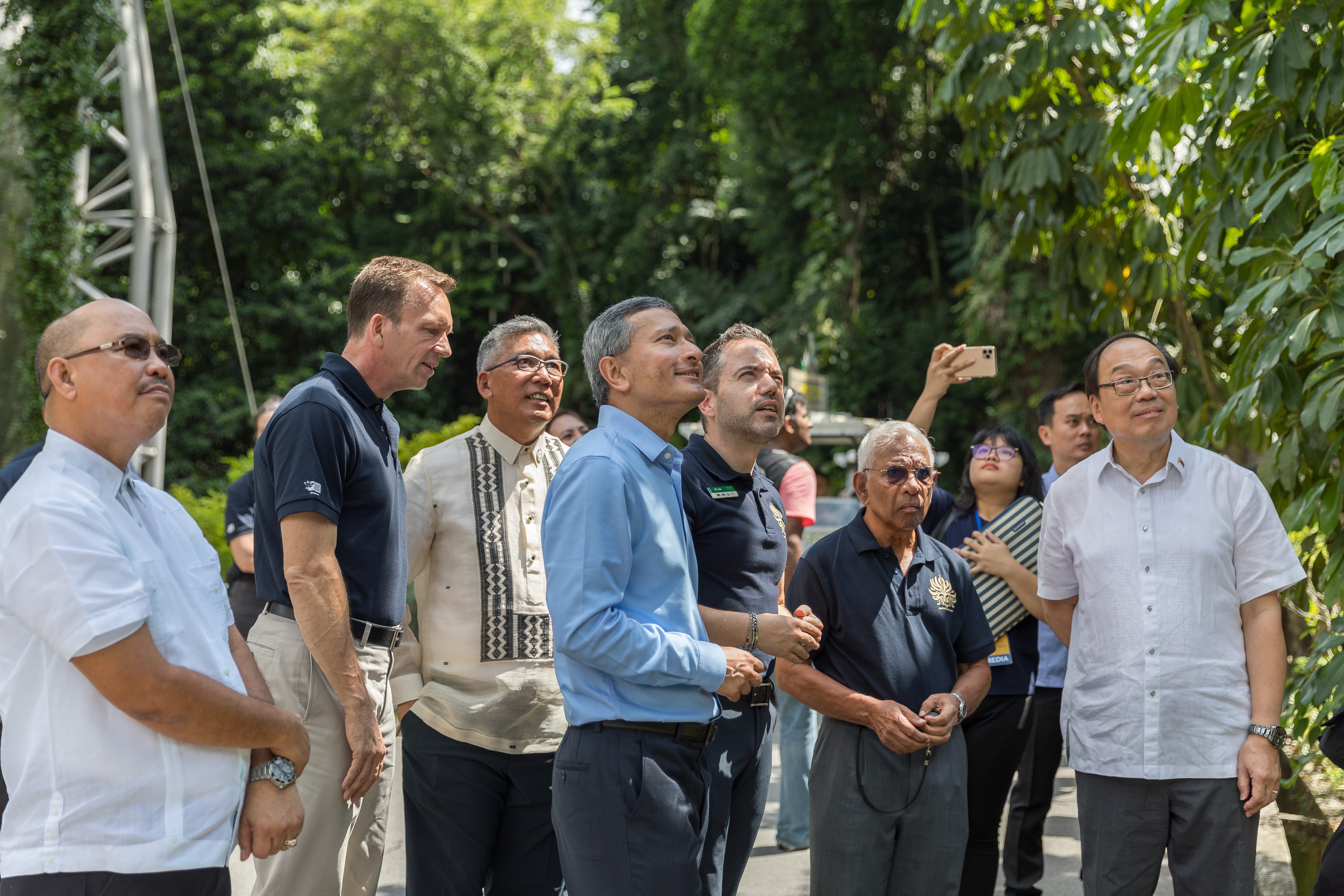 Group of people outdoors, looking up. Someone is holding a phone up as if taking a photo.
