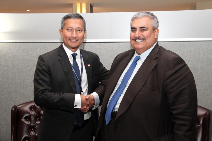 Two men in suits shaking hands in front of an office wall.