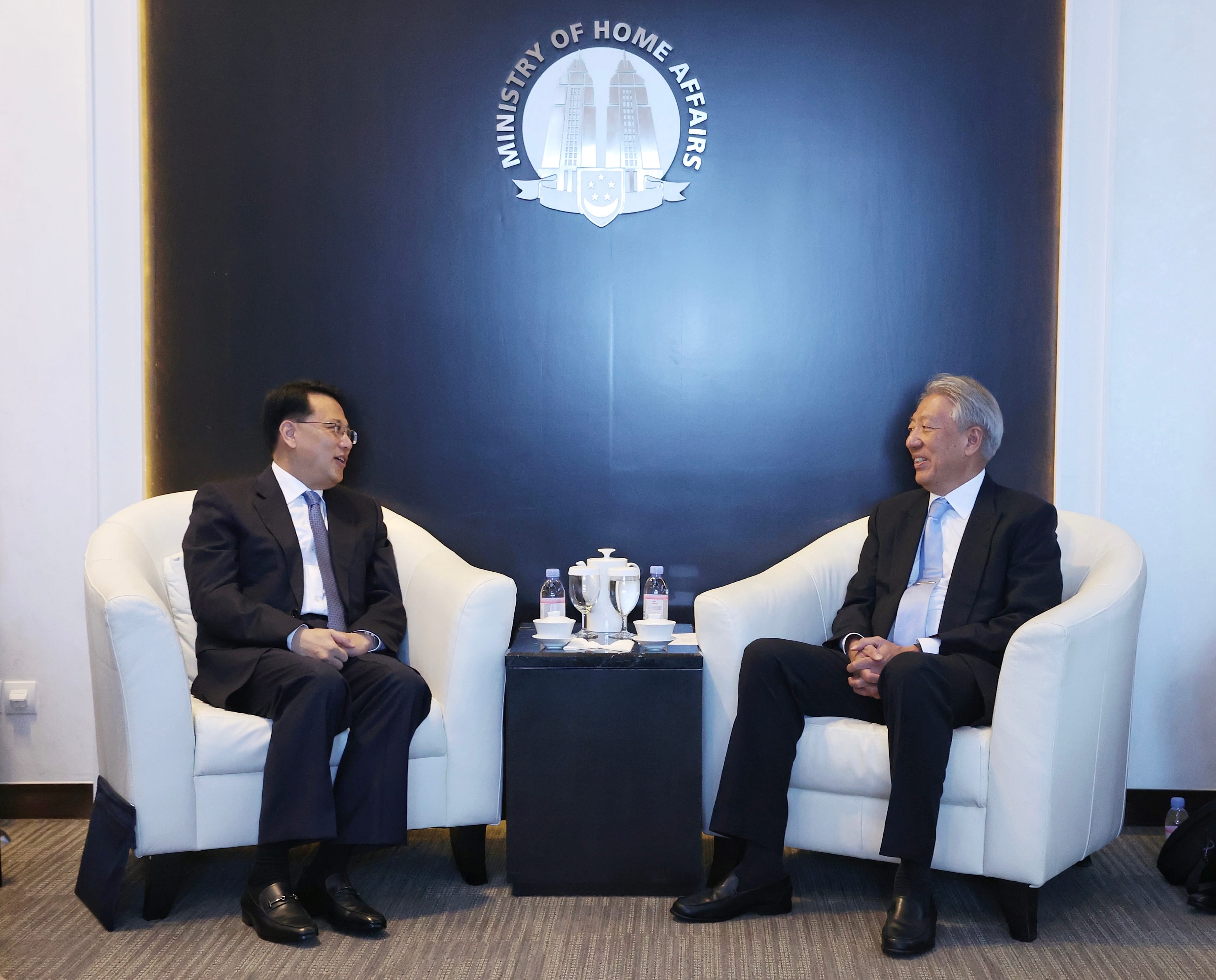 Eight people in business attire stand in front of a blue screen and plants.