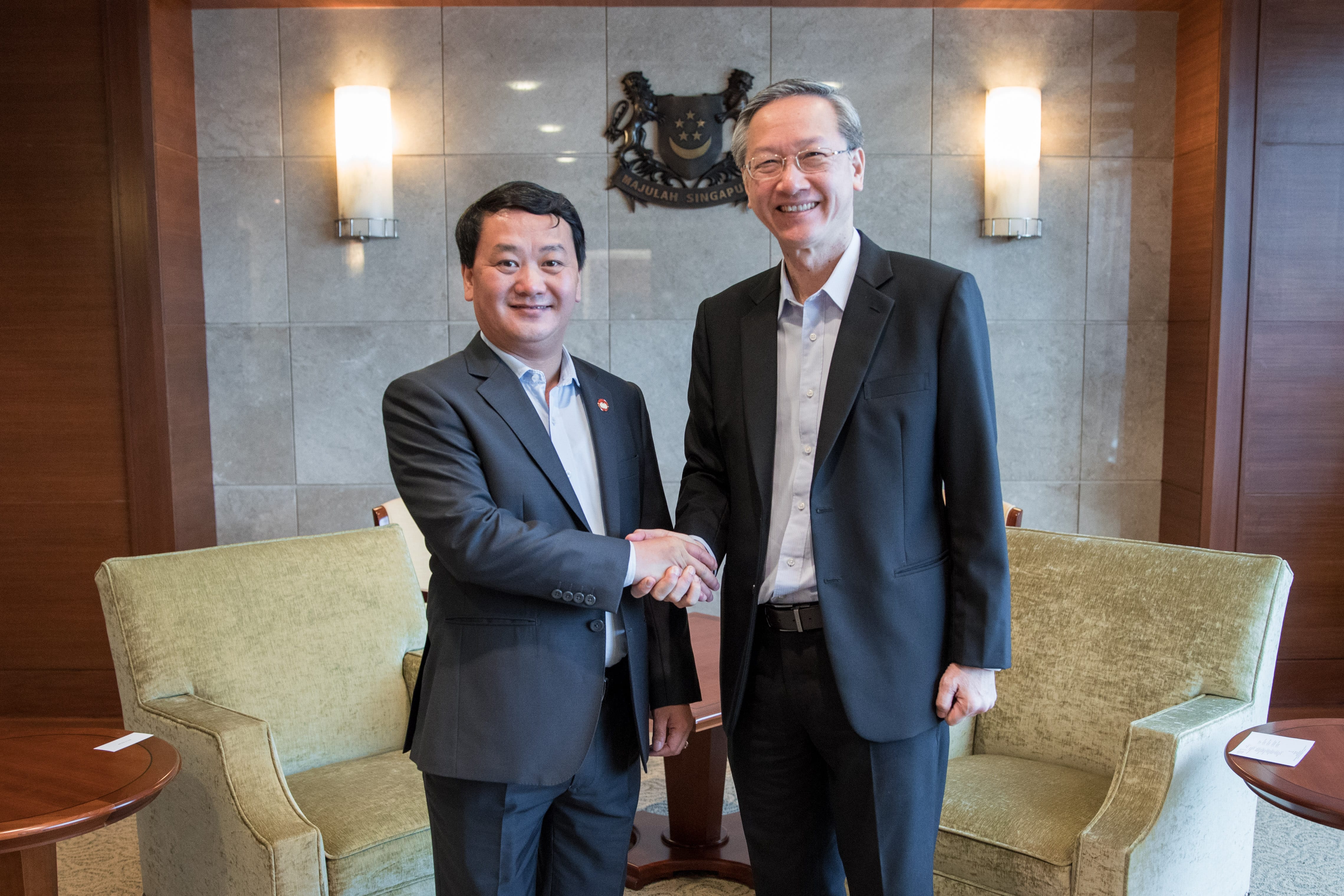 Two men in suits shaking hands in front of the Singapore coat of arms.